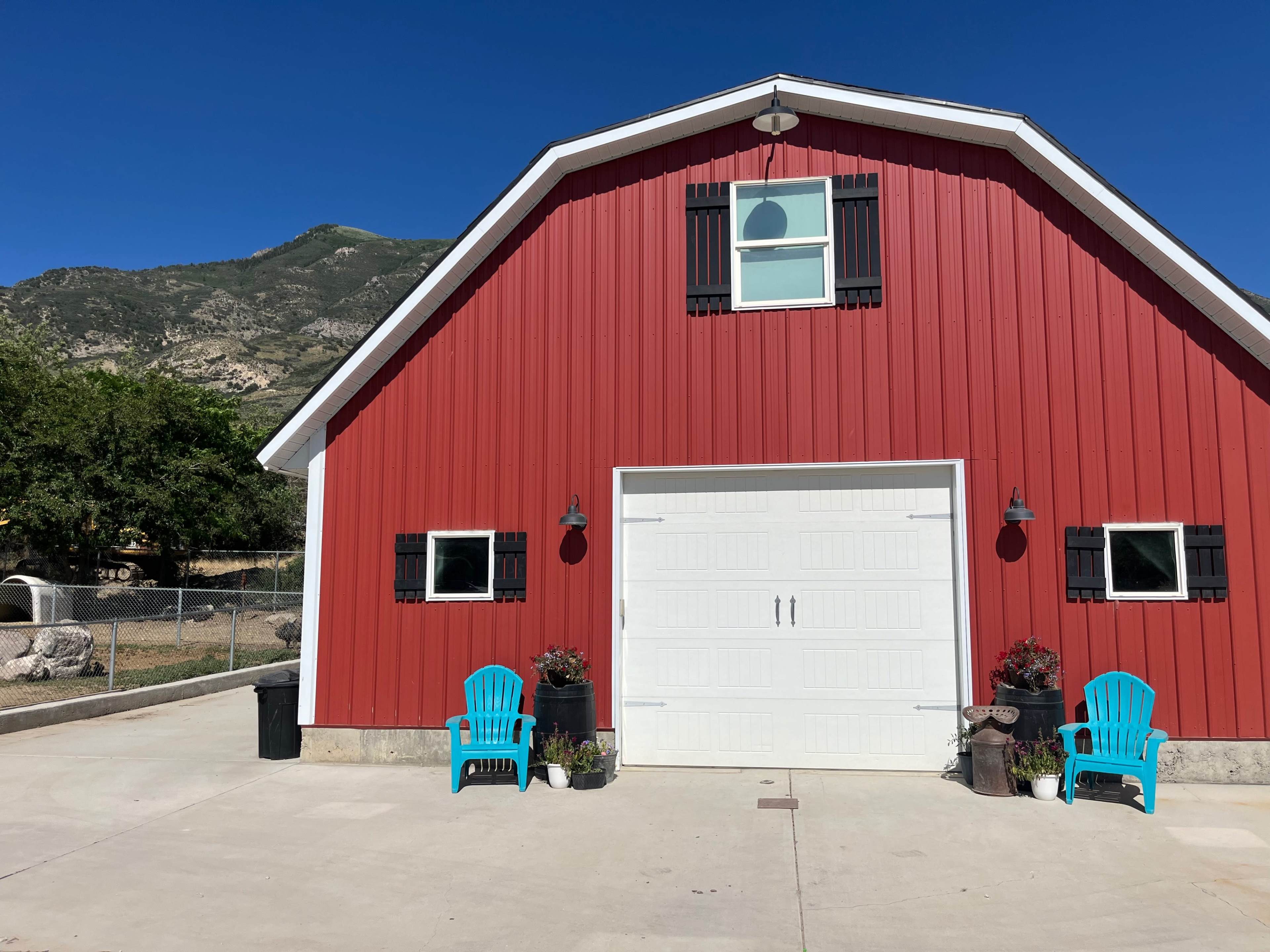 A red barn with a white garage door and two blue chairs is set against a mountainous backdrop.
