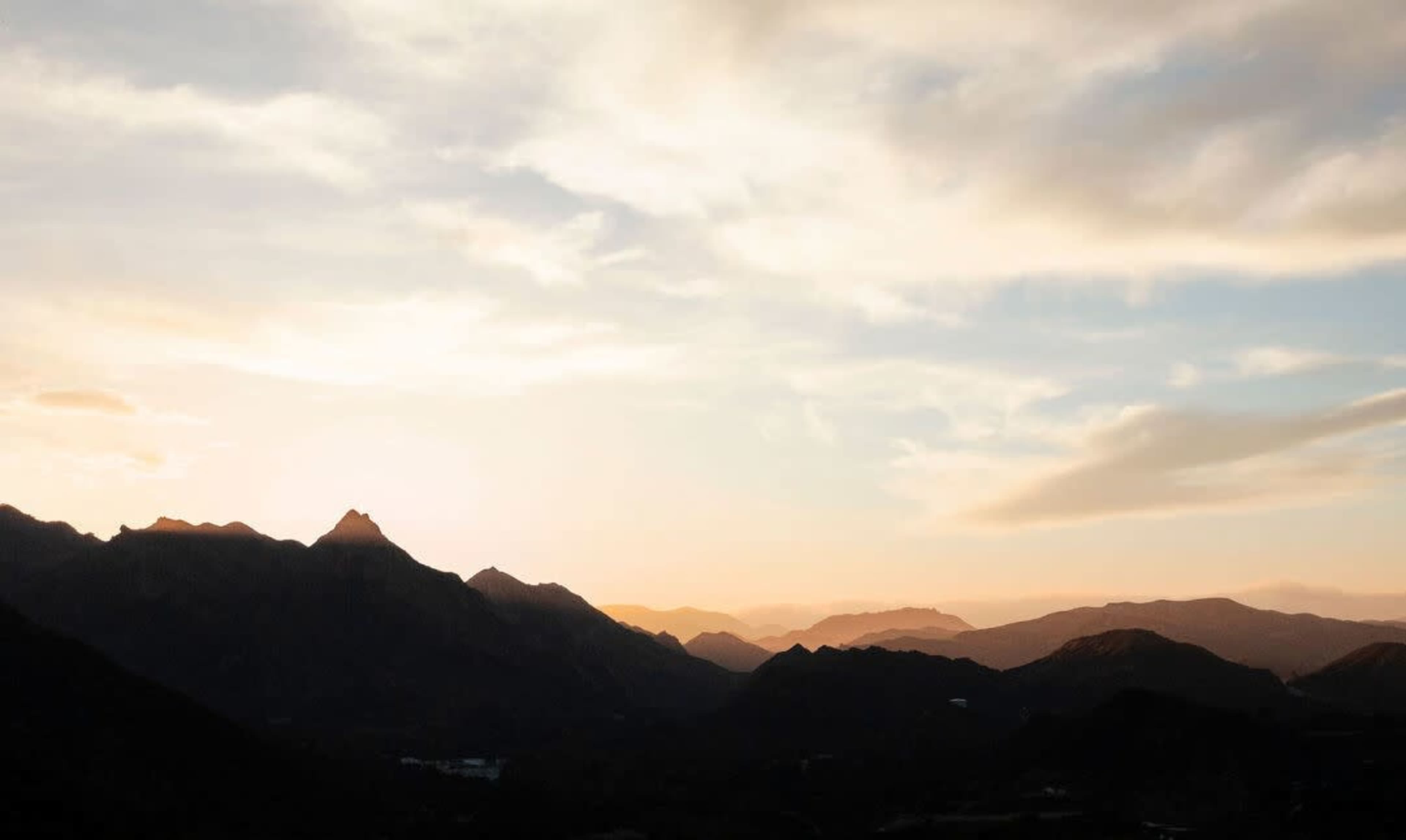 A range of mountains under a sky filled with soft clouds during sunset.