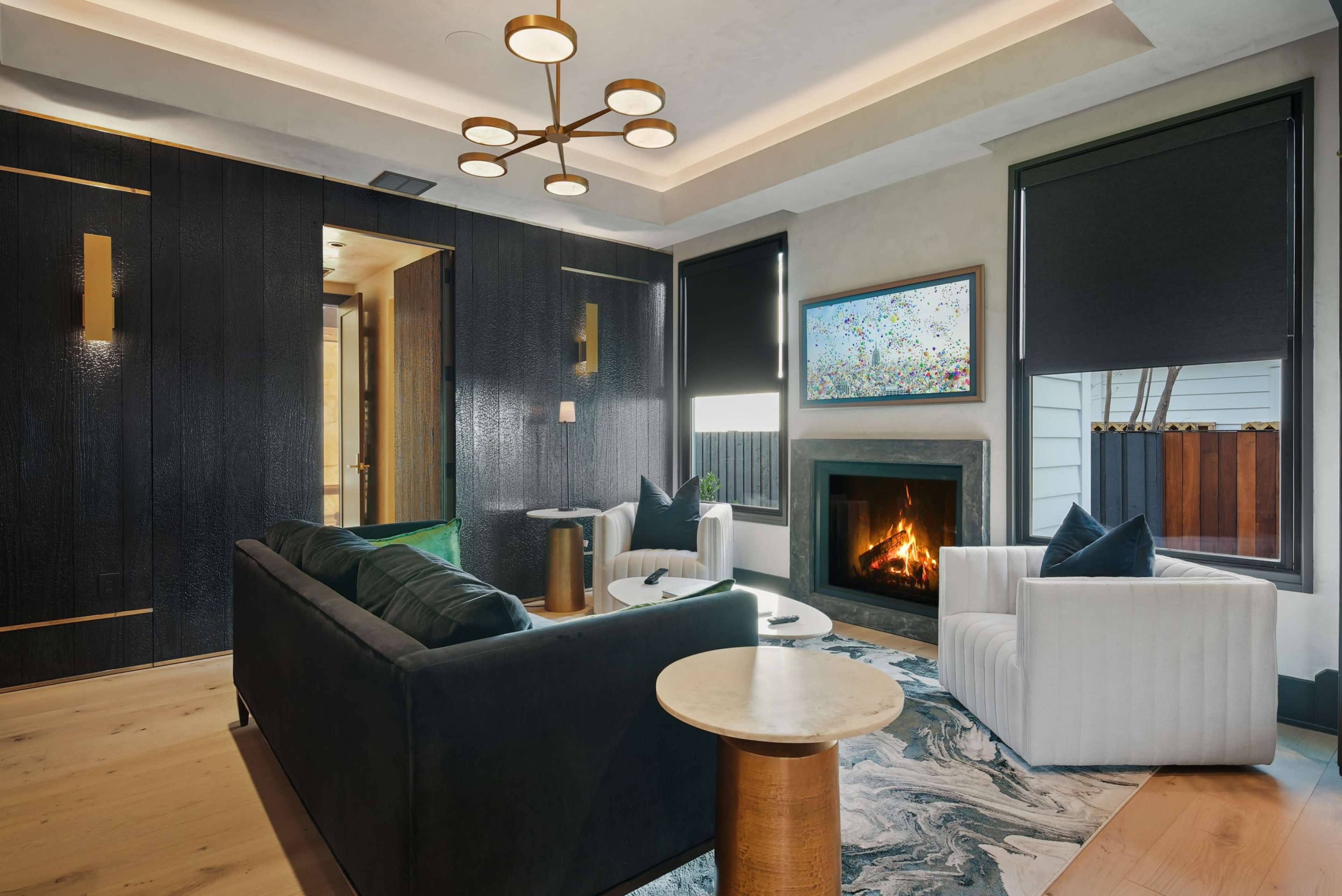 A modern living room features dark walls, two sofas, a coffee table, a fireplace, and a large artwork on display.