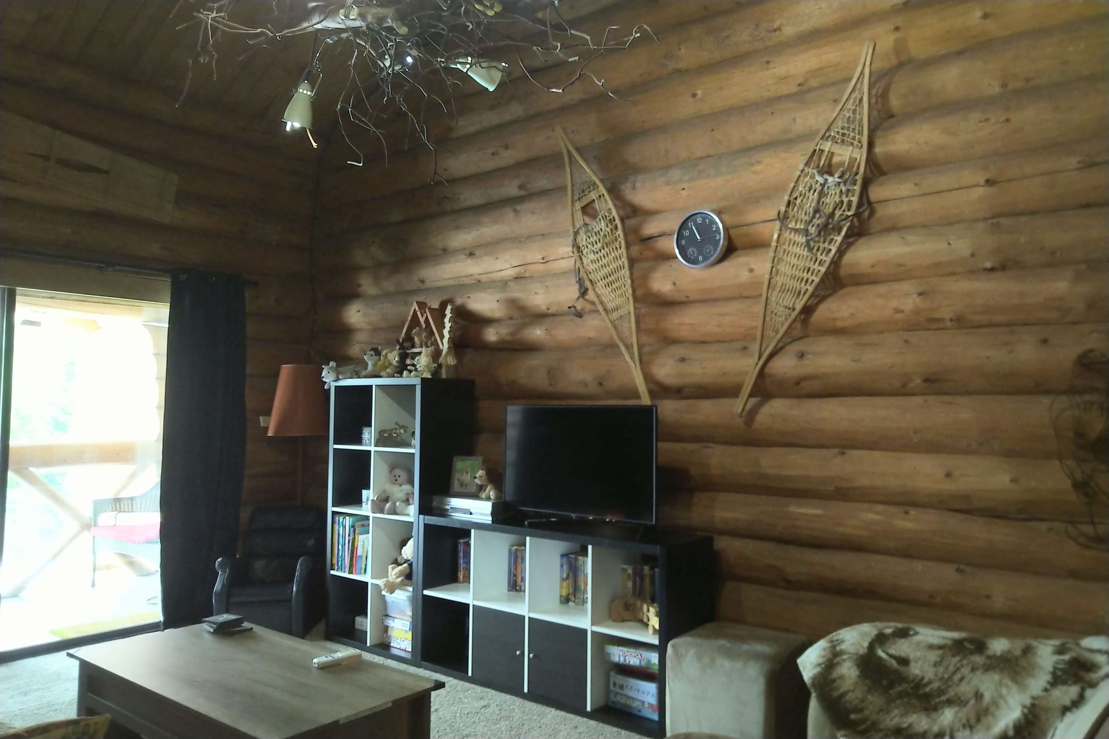 A log cabin interior featuring a bookshelf, a television, and snowshoes mounted on the wall.
