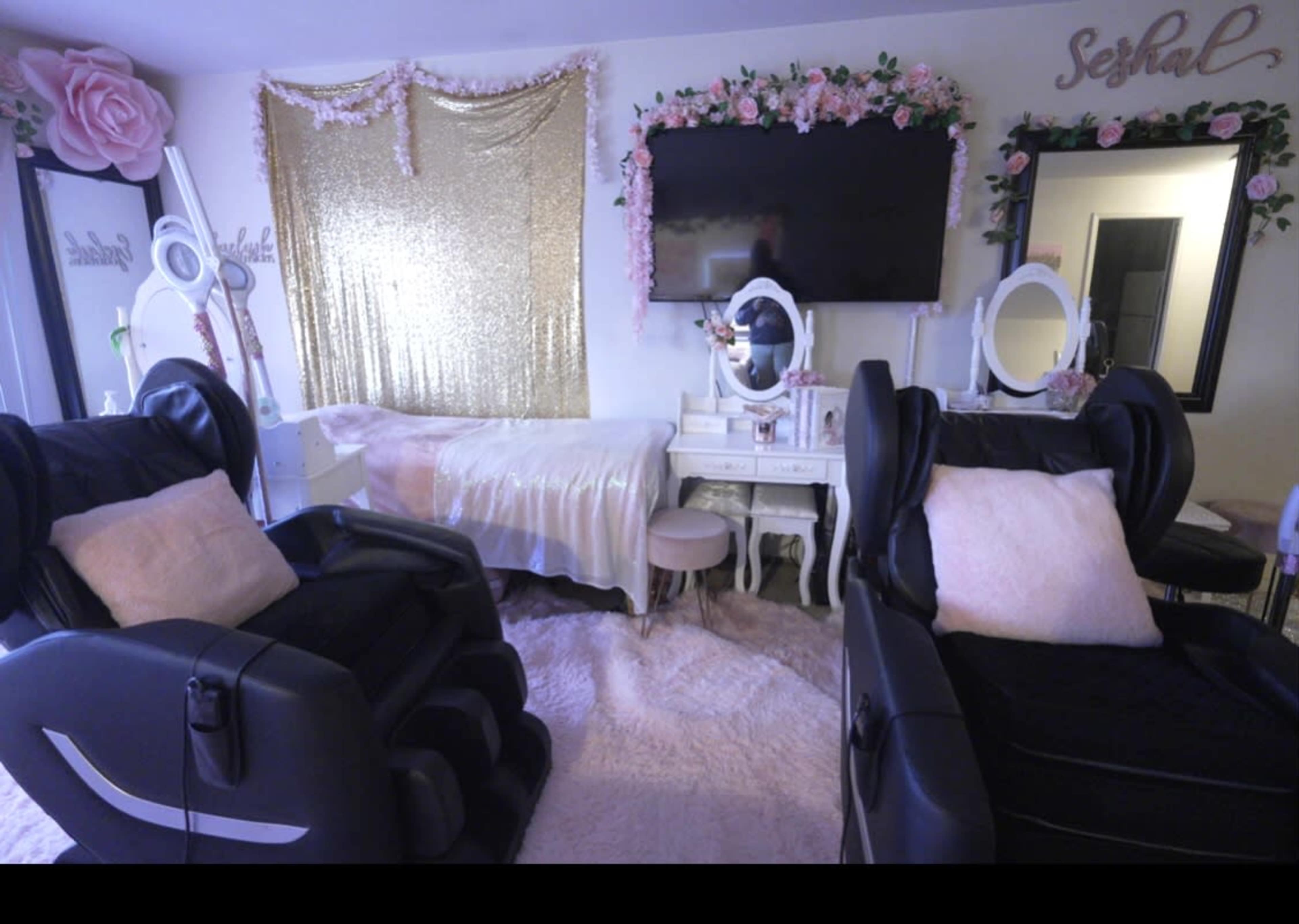 A beauty treatment room featuring two black massage chairs, a gold sequined backdrop, and a decorative mirror with floral accents.