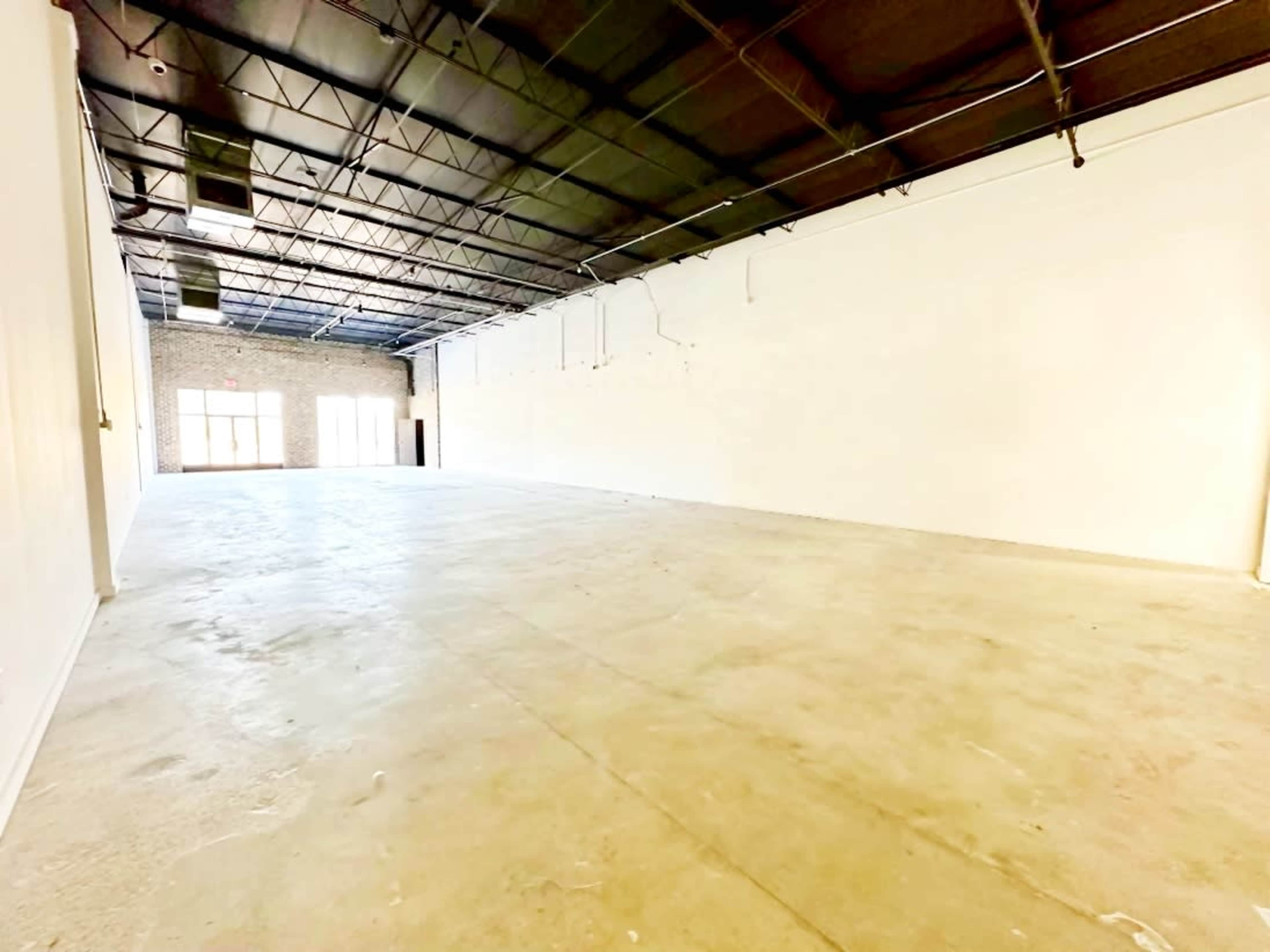The image shows a large, empty indoor space with concrete flooring and blank white walls.