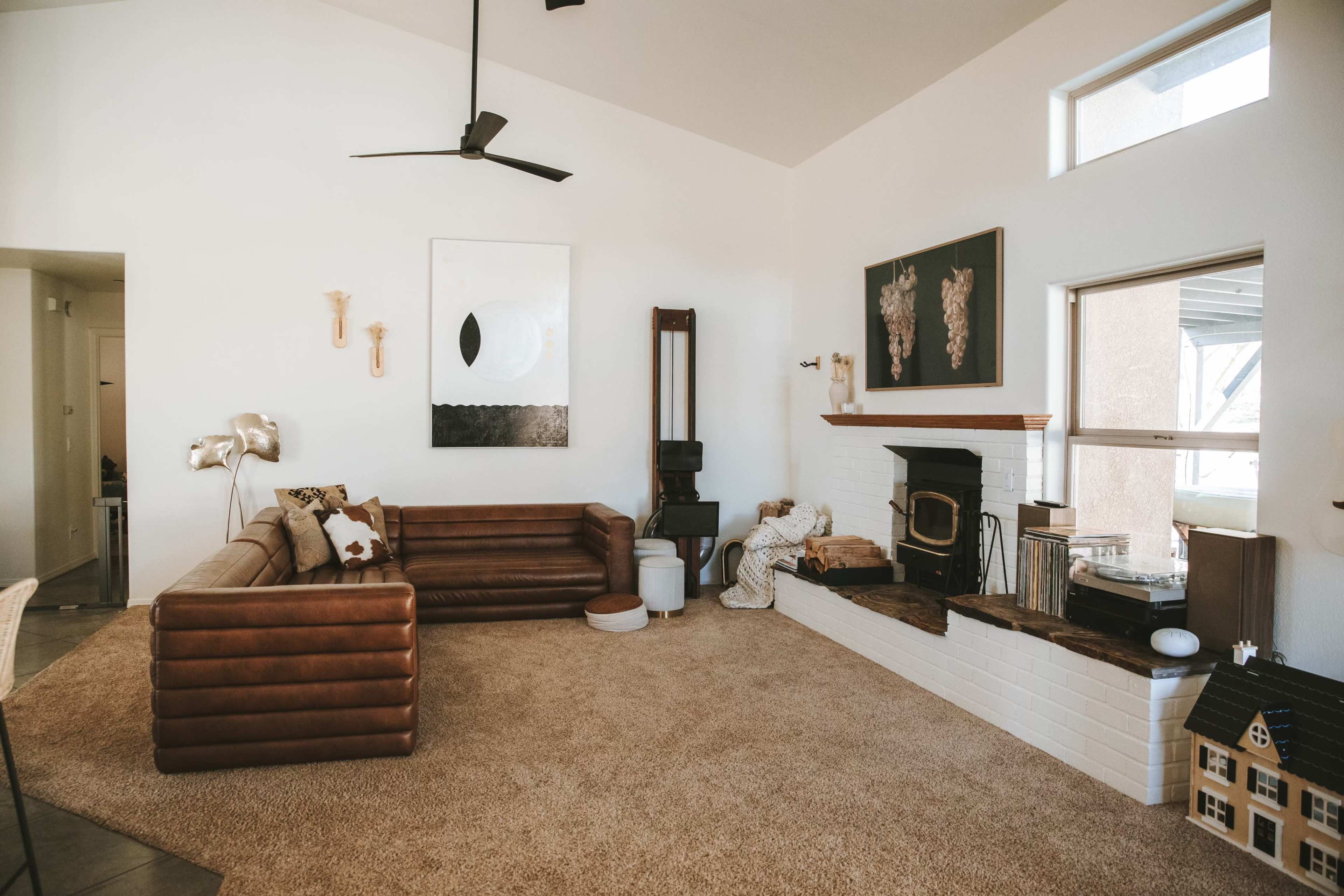 The spacious living room features a brown leather sofa, a white brick fireplace, and modern artwork on the walls.