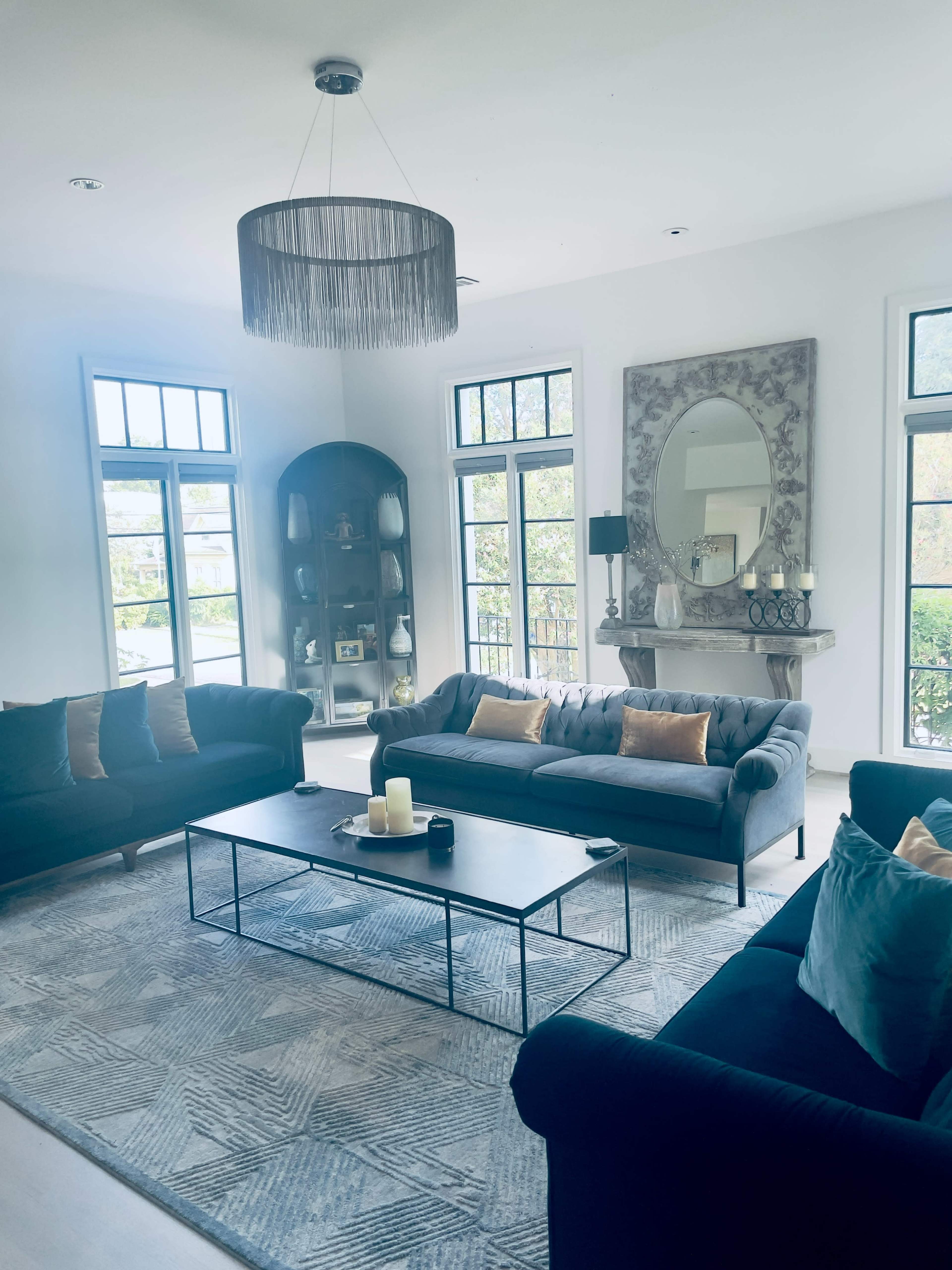 The scene features a modern living room with two dark sofas, a coffee table in the center, and large windows allowing natural light to fill the space.