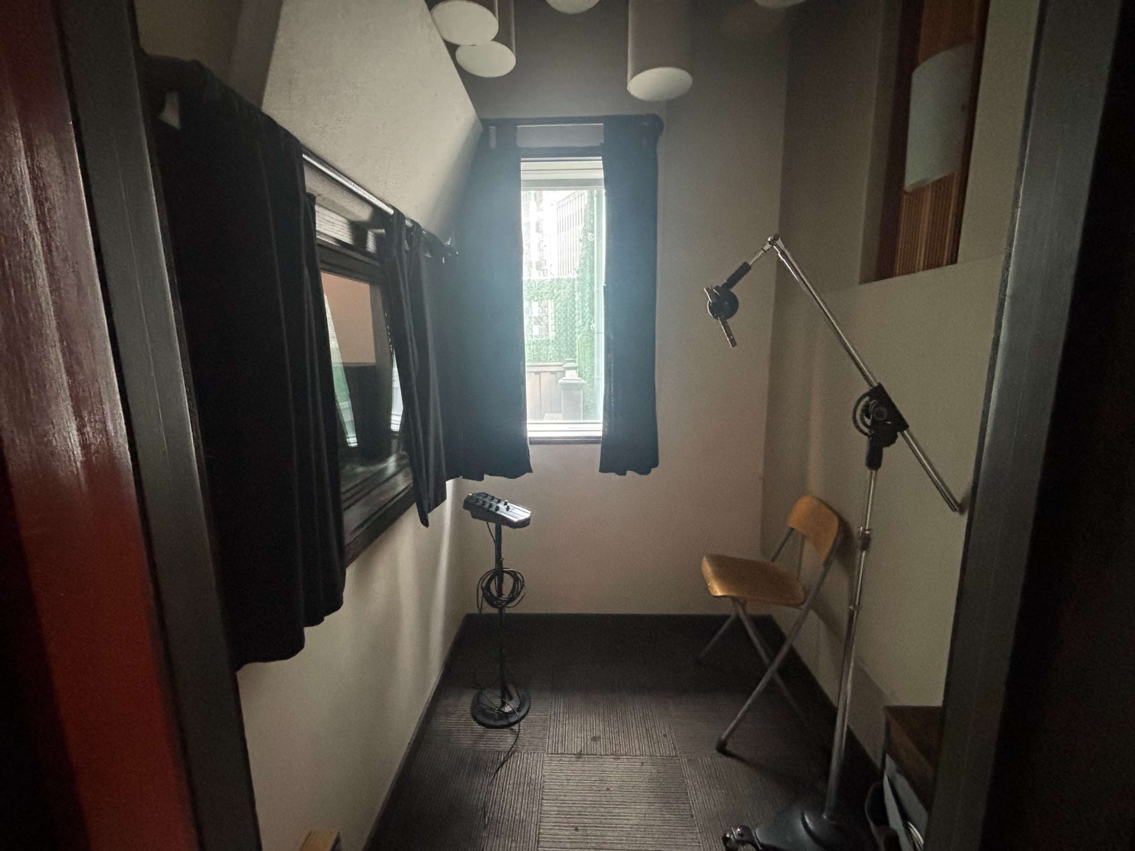 The image shows a small room with a window, a chair, a microphone stand, and a mirror on the wall.