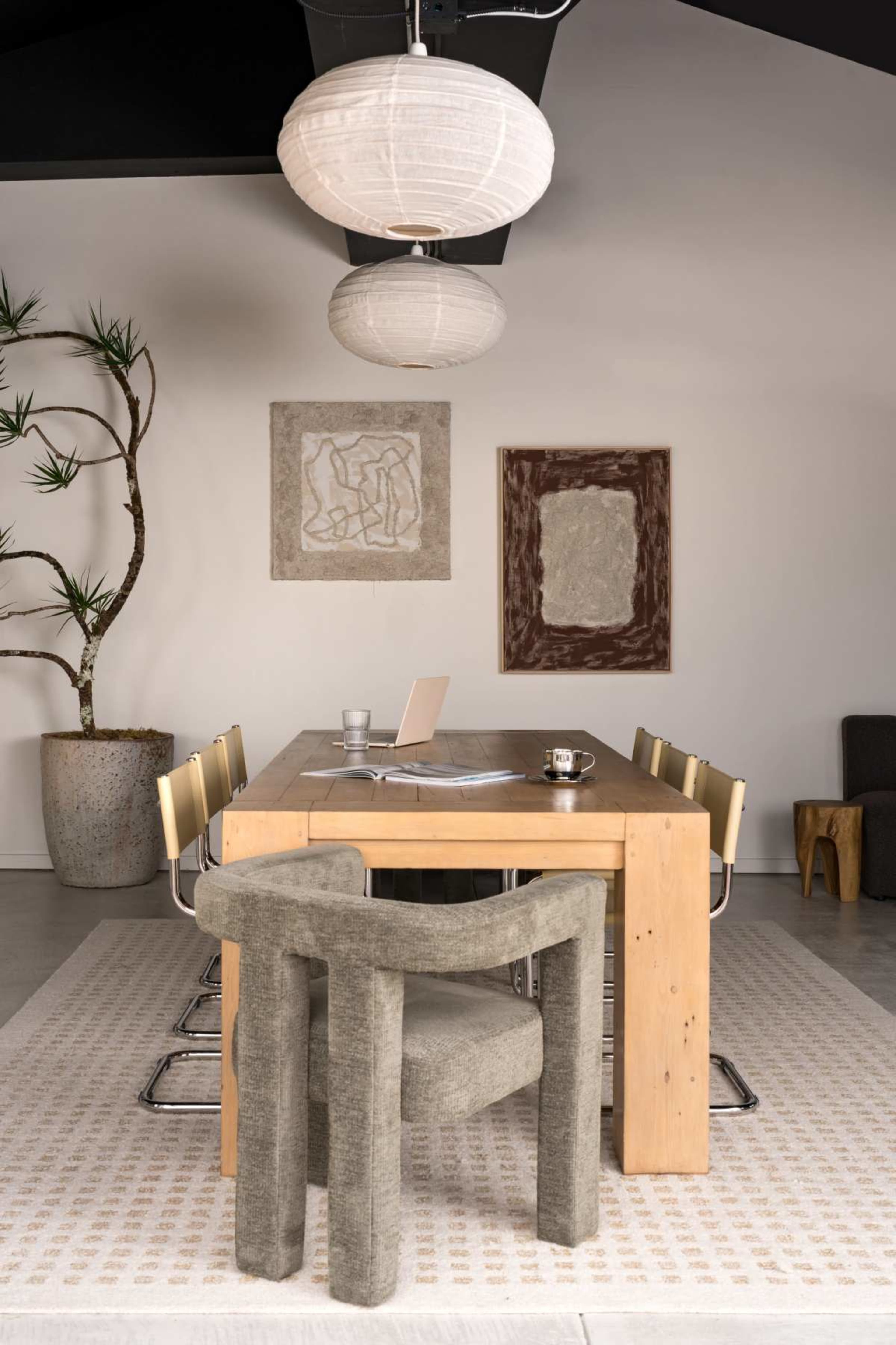 The image shows a modern dining room with a wooden table surrounded by chairs, two pendant lights above, and artwork displayed on the walls.