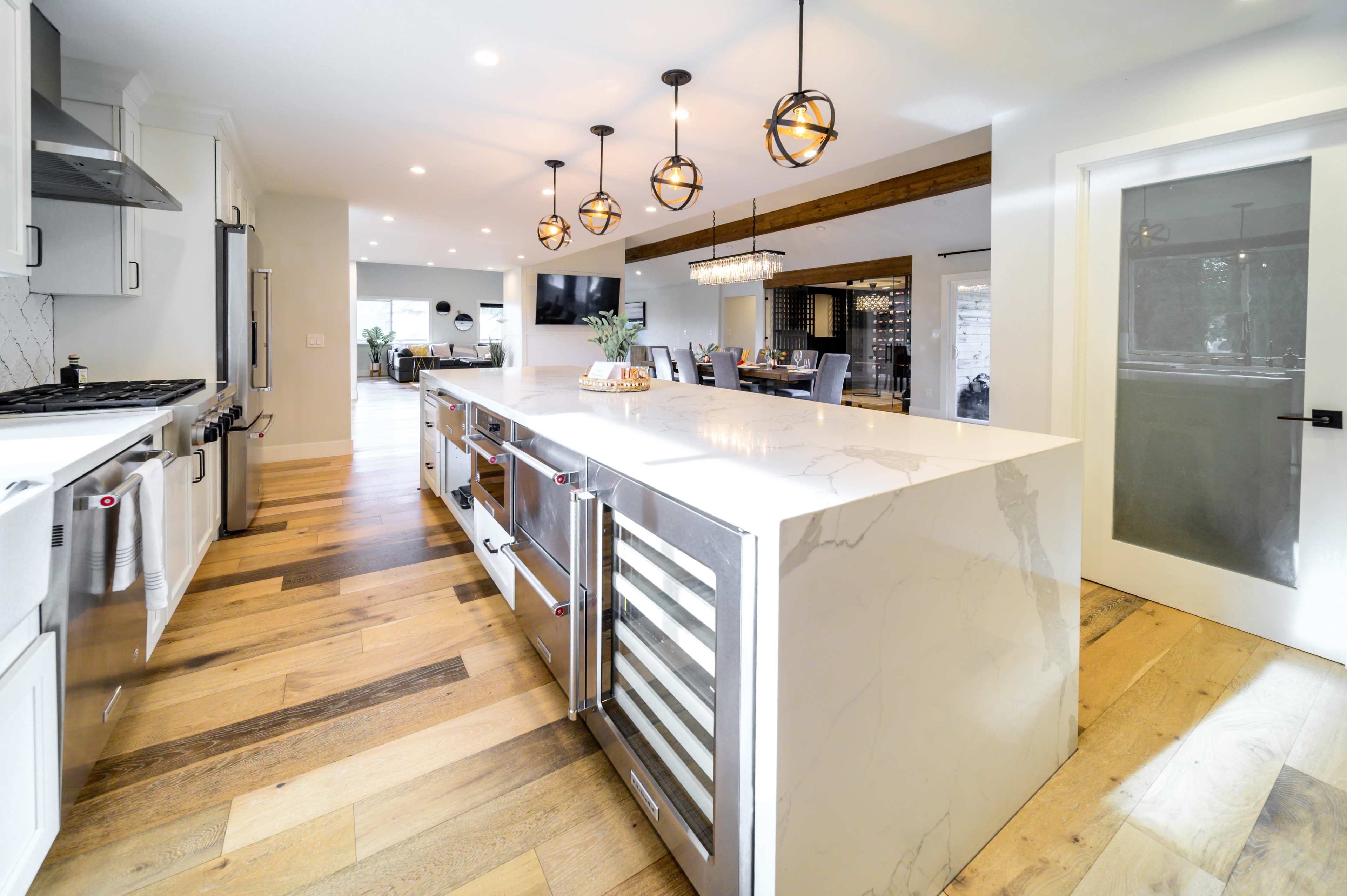 A modern kitchen features a large island with marble countertops, pendant lights overhead, and stainless steel appliances.