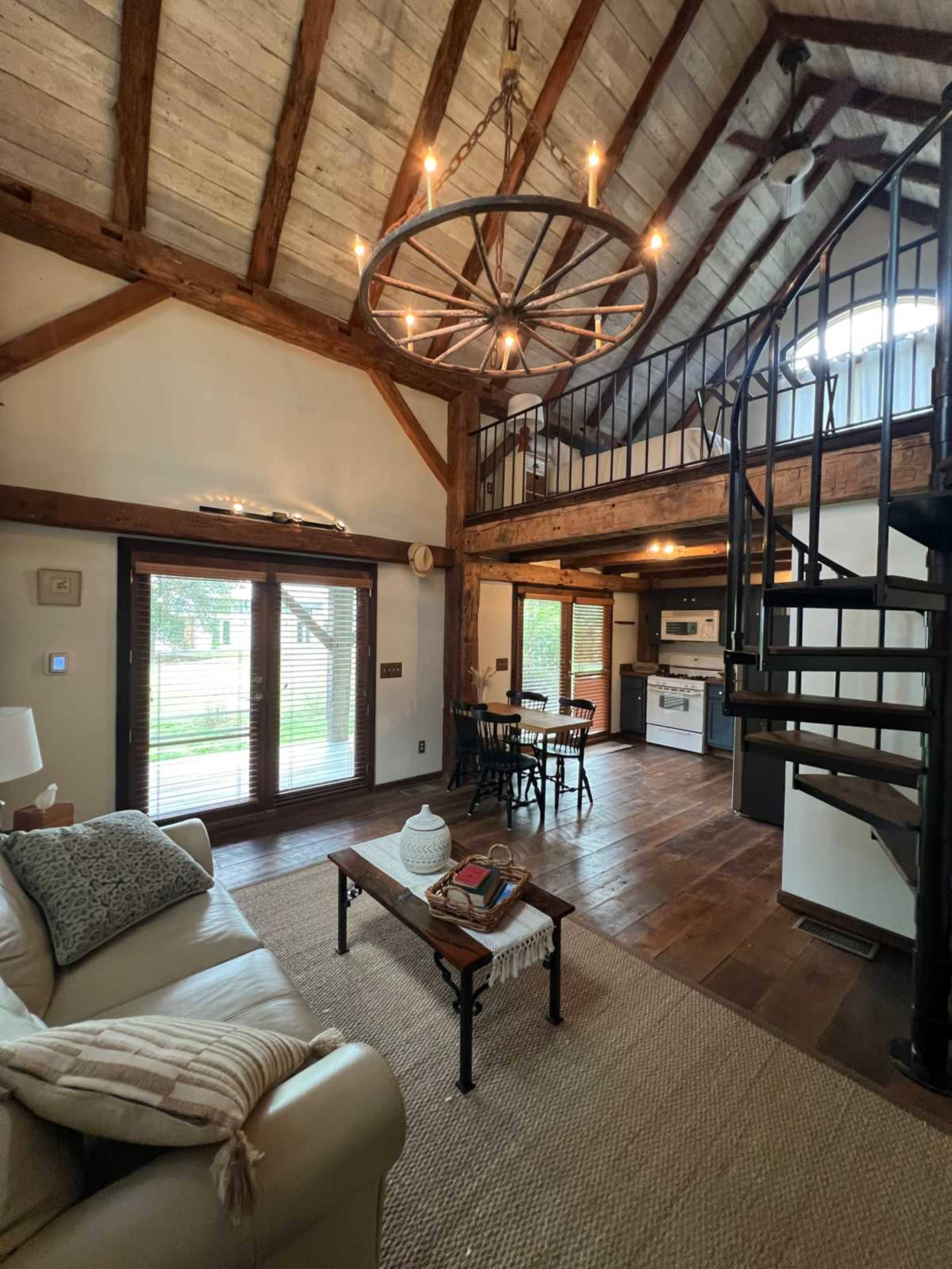 The interior of a rustic-style home showcases a living area with wooden beams, a spiral staircase, a kitchen, and a seating arrangement.