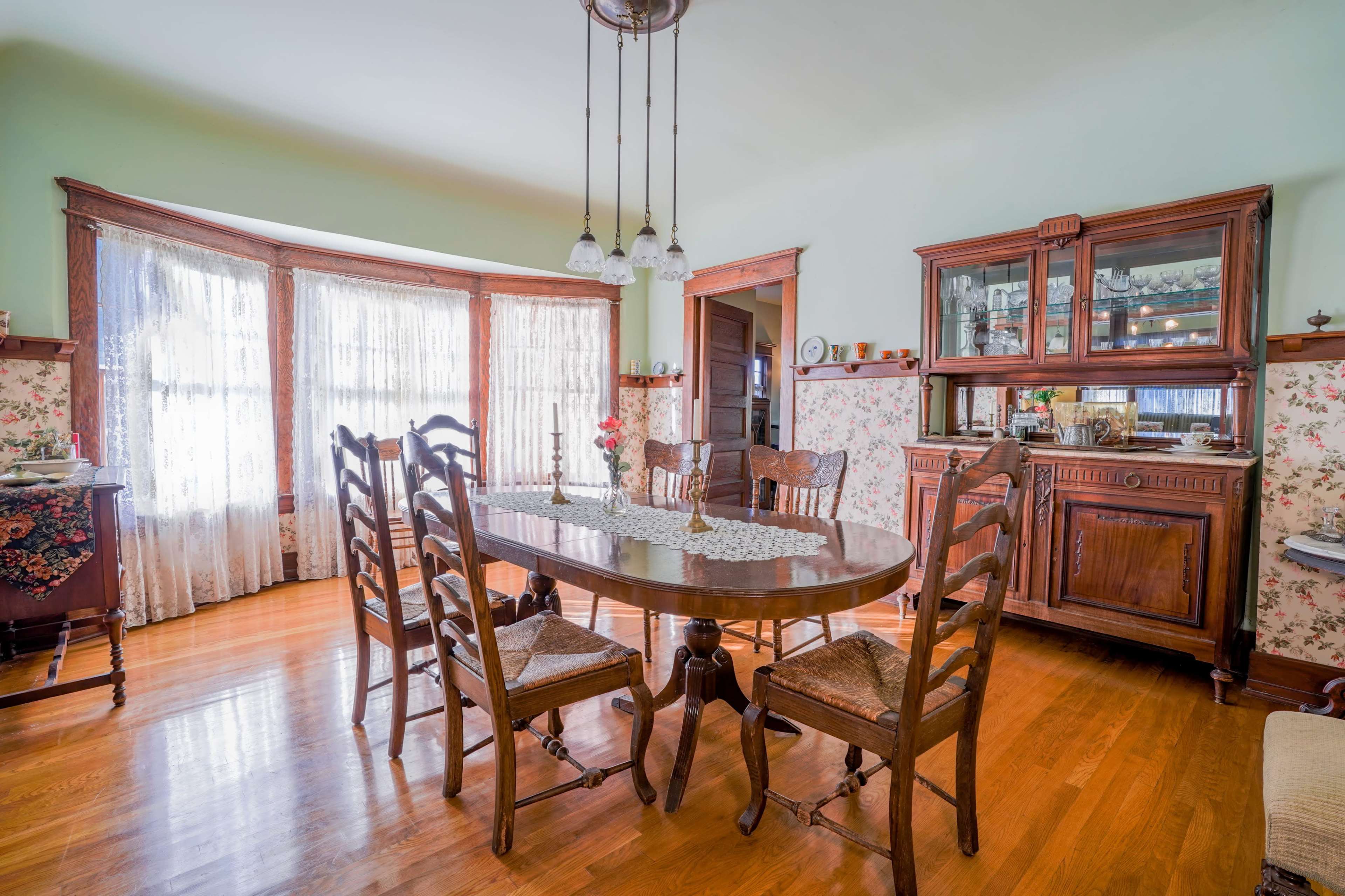 The dining room features a wooden table surrounded by chairs, with a china cabinet and floral wallpaper accentuating the space.
