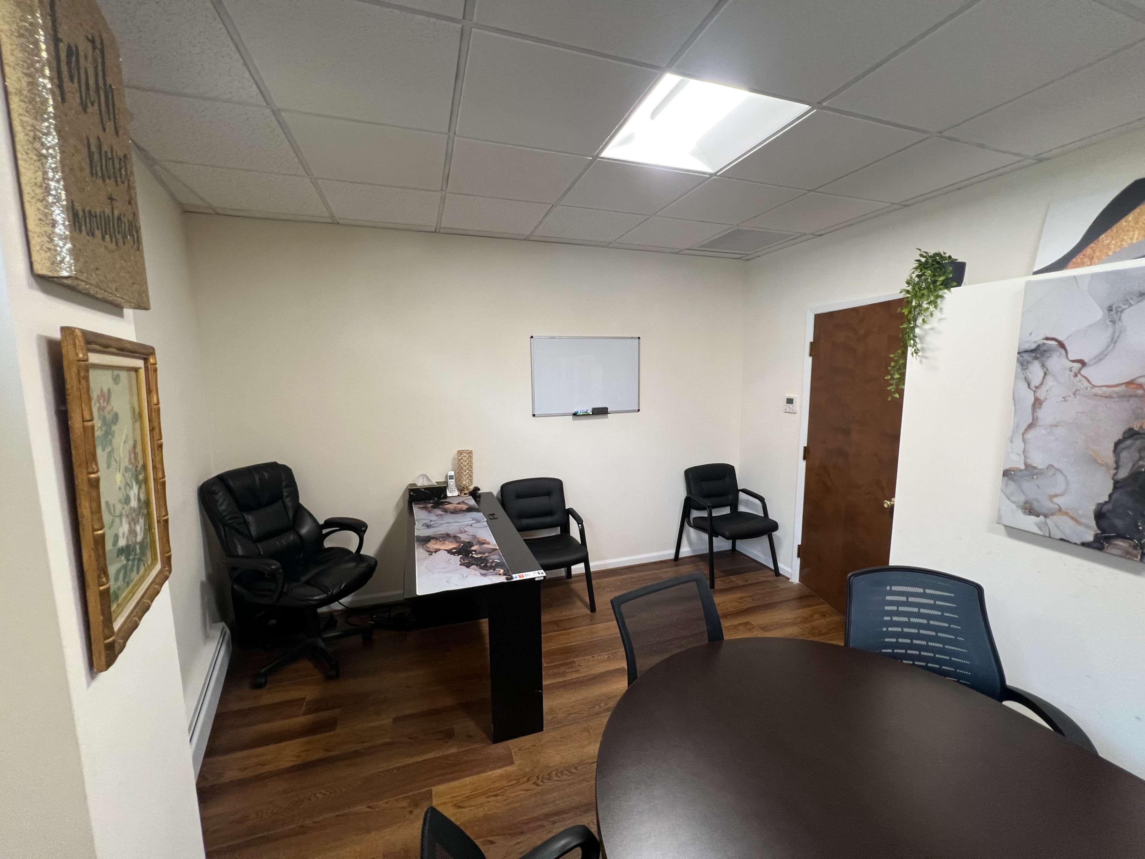 A small office space with a desk, chairs, a round table, and a whiteboard on the wall.