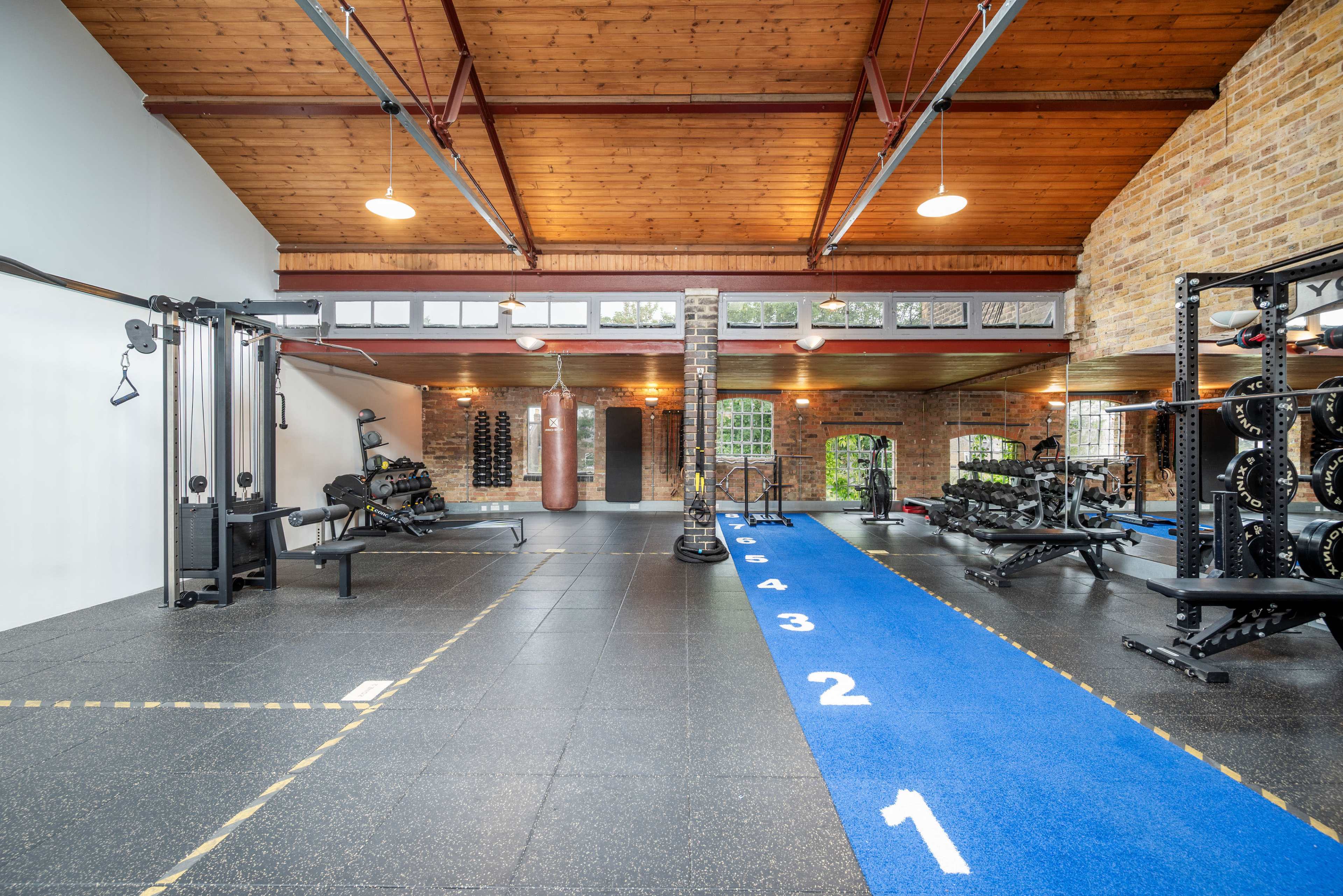 The image shows a spacious gym featuring various workout equipment, a punching bag, and a marked blue track along the floor.