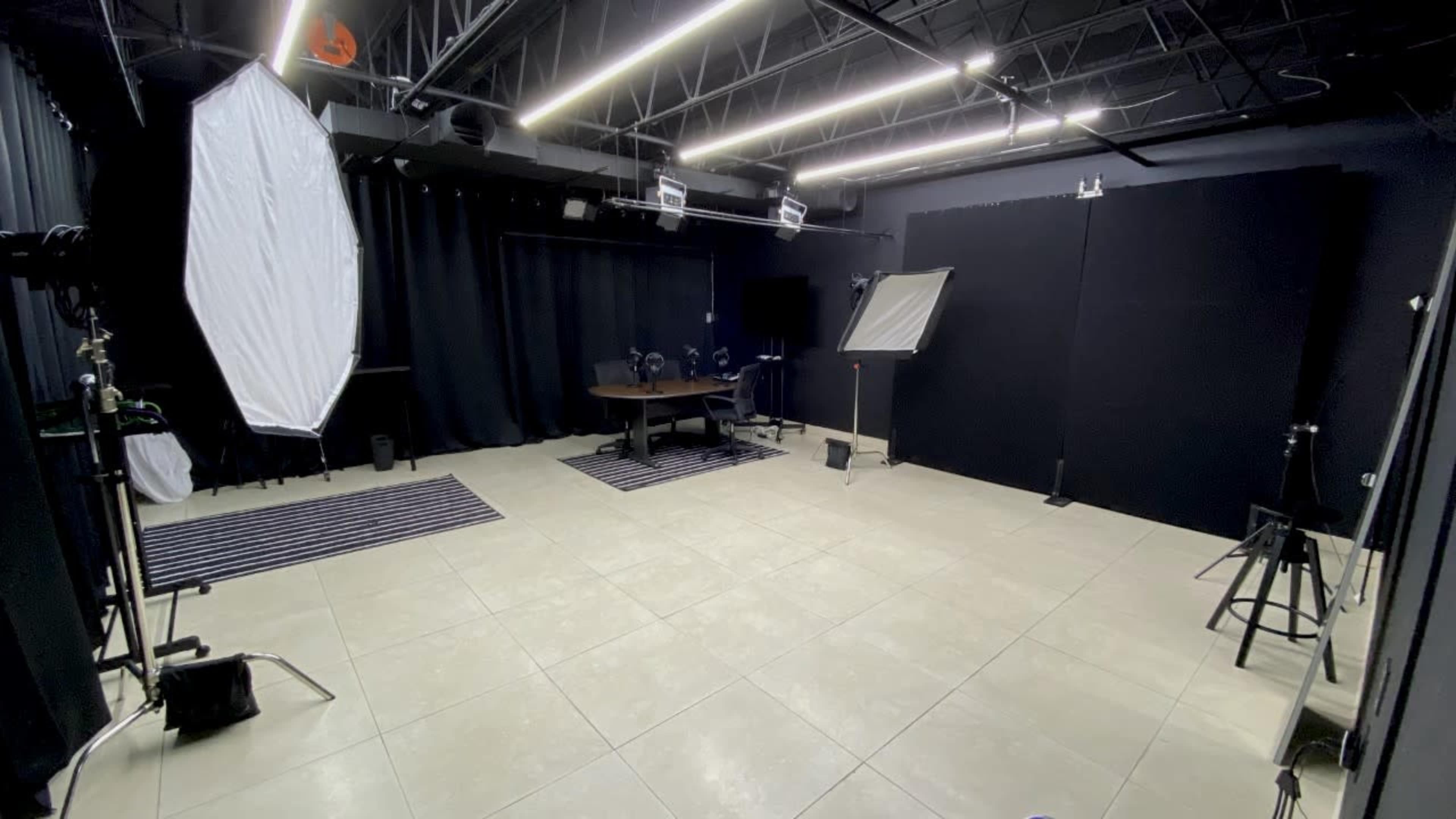 A photography studio featuring a central table, multiple lighting setups, and black curtains along the walls.