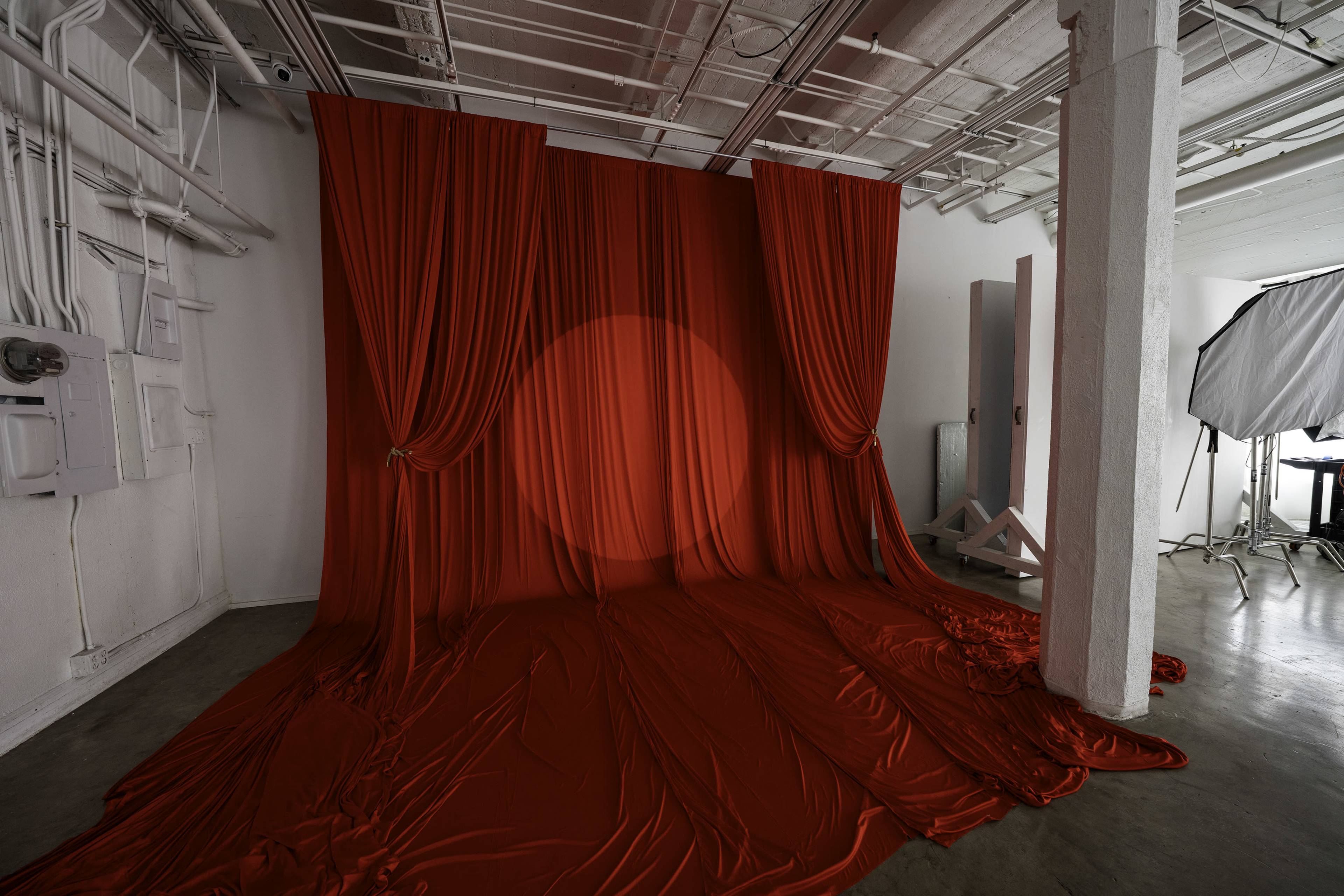 The image features a studio space with a backdrop of red fabric draped across the wall and floor, creating a seamless red environment.