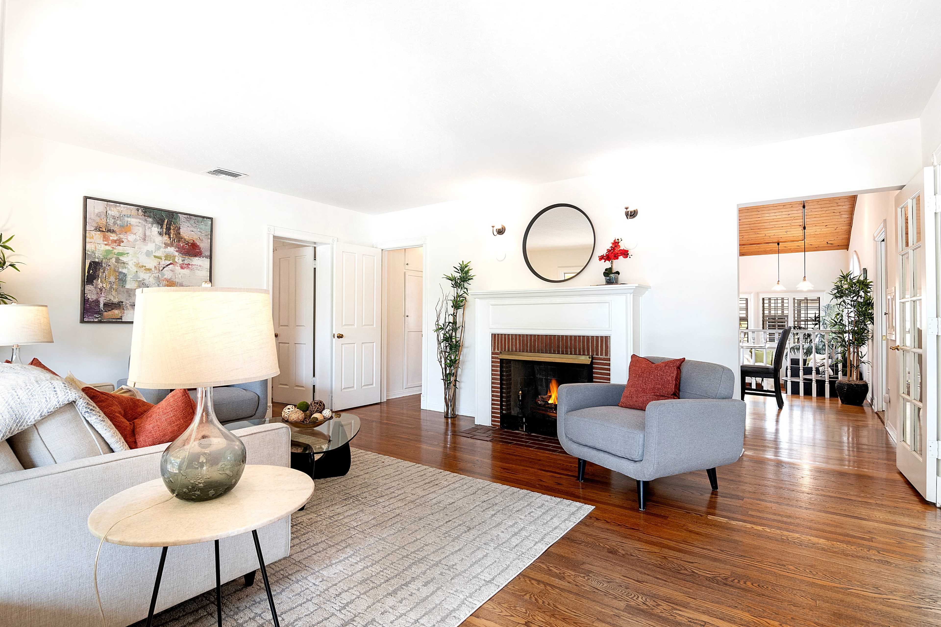 The living room features a gray sofa, a round coffee table, and a fireplace, with a view into an adjacent dining area through double doors.