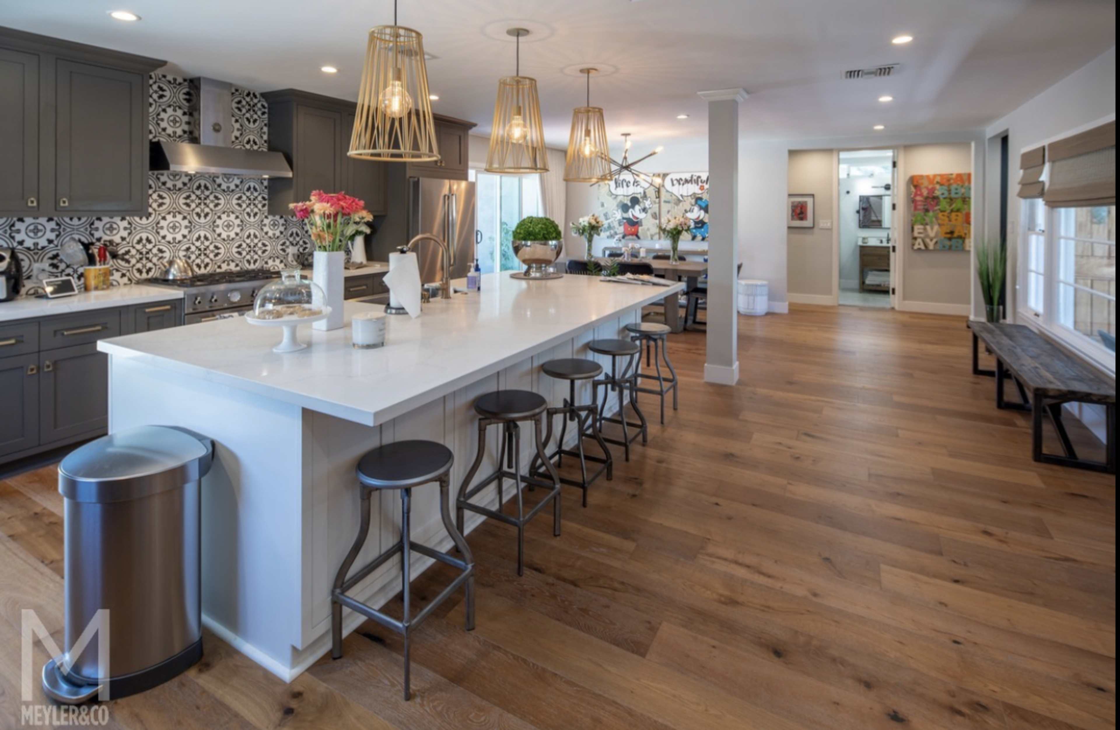 A spacious kitchen features a large island with bar stools, modern cabinetry, and decorative tile backsplash.