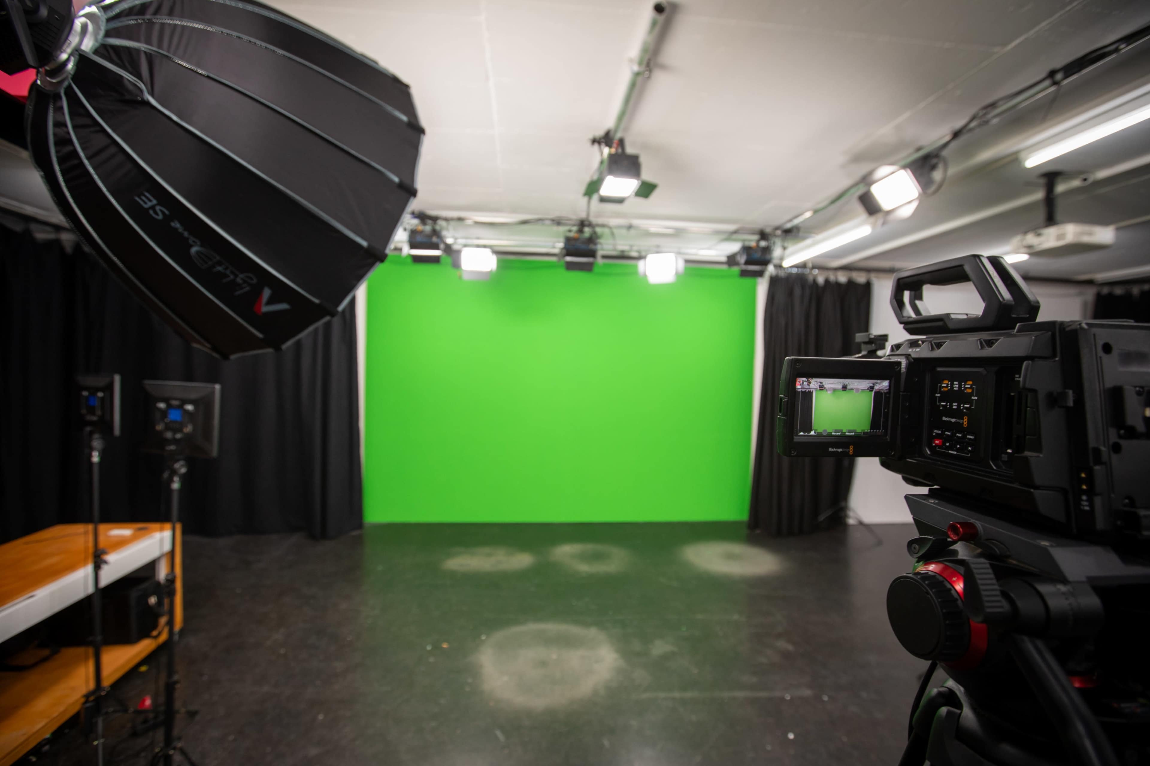 A professional video production studio features a green screen backdrop, a camera focused on the green area, and multiple lights set up for filming.