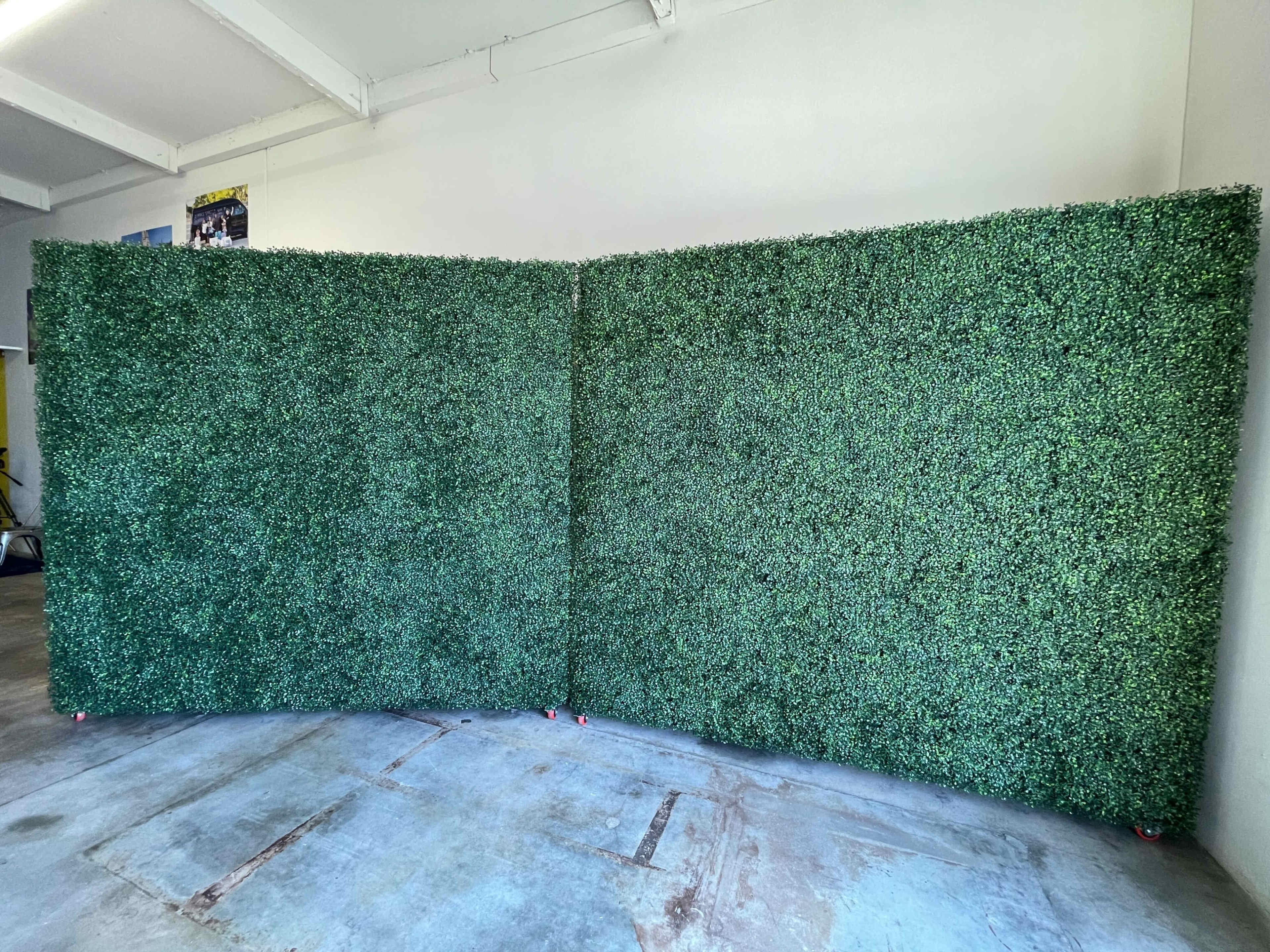 A large, artificial greenery wall set up in a room with a concrete floor.