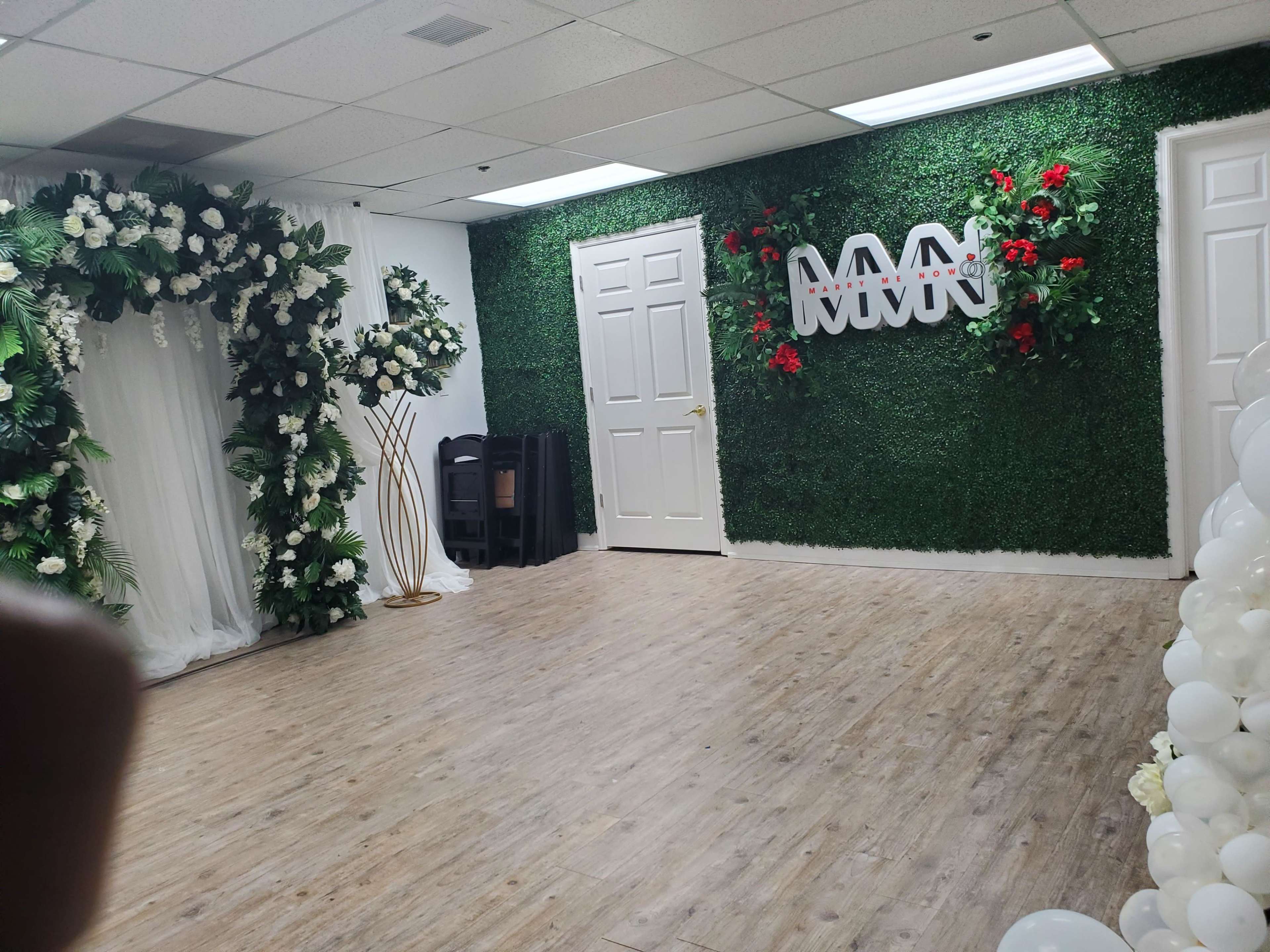 A decorated indoor space featuring a green wall with floral arrangements, a wooden floor, and a logo on the wall.