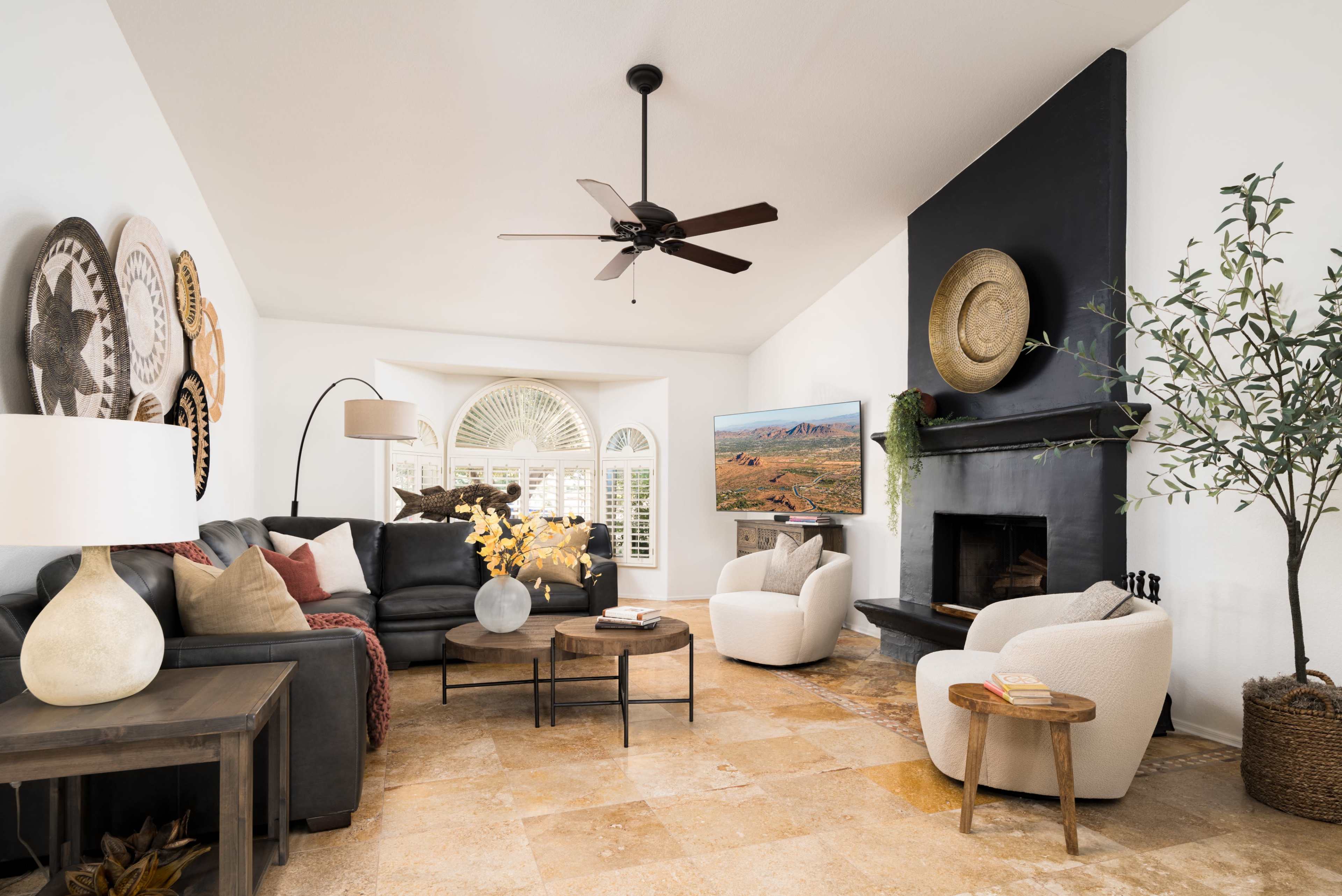 A modern living room features a black fireplace, large windows, two armchairs, a coffee table, and wall-mounted artwork.