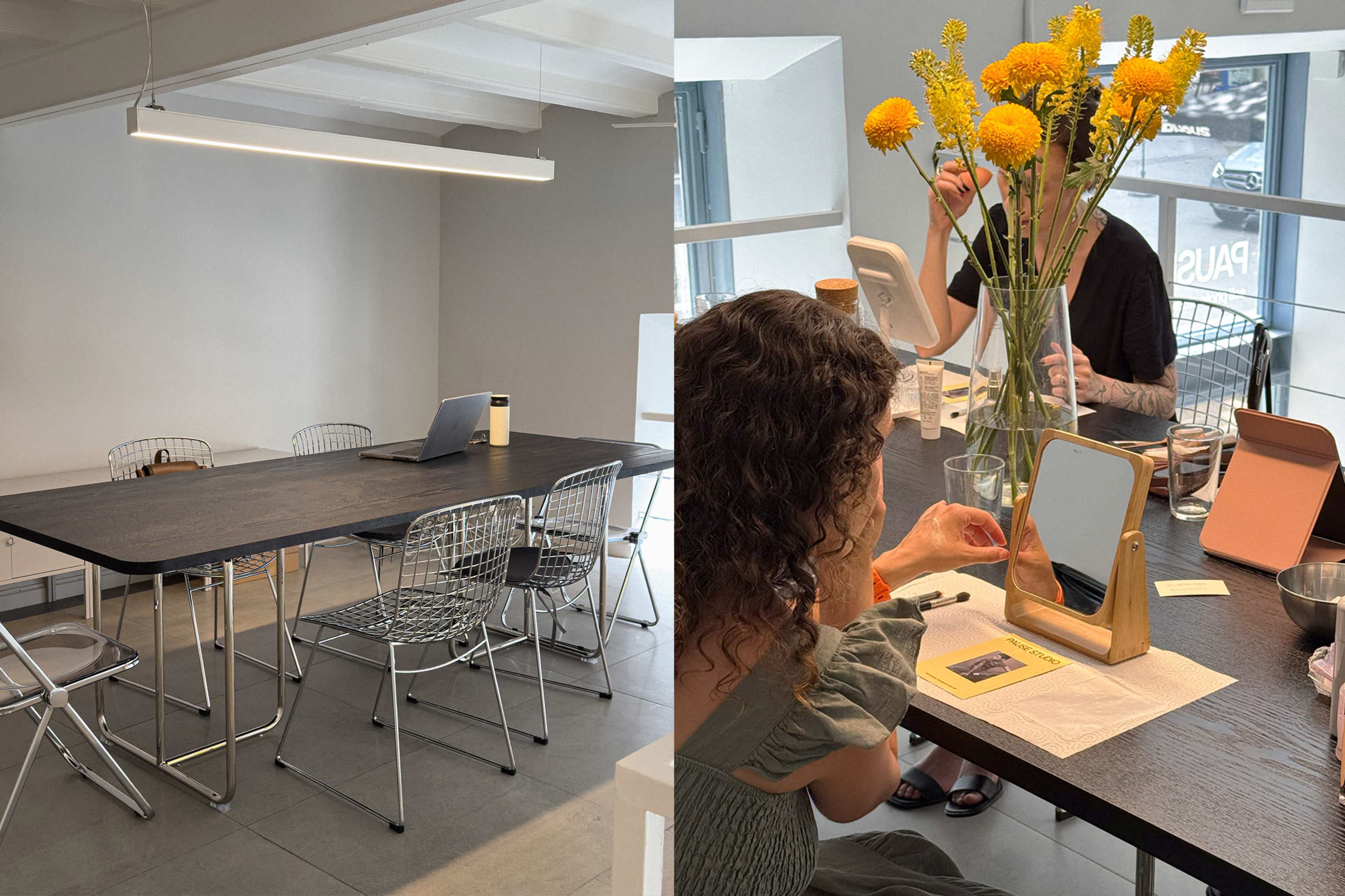 A spacious, modern room features a large table surrounded by wire chairs, and a person sitting at the table interacts with a mirror and floral arrangement.