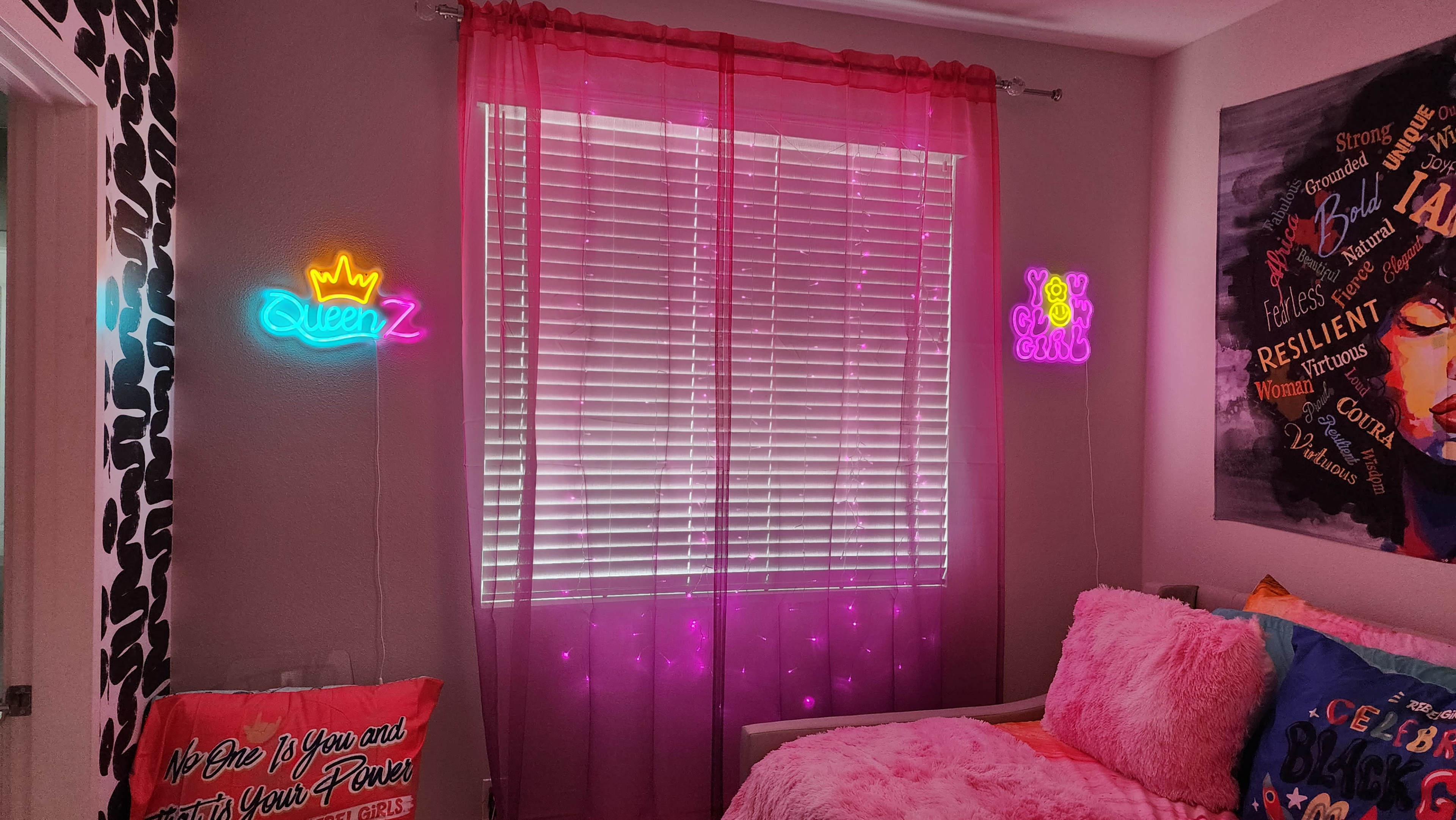 A brightly decorated room features neon signs that read "Queen" and "Girl," alongside pink curtains and colorful bedding.