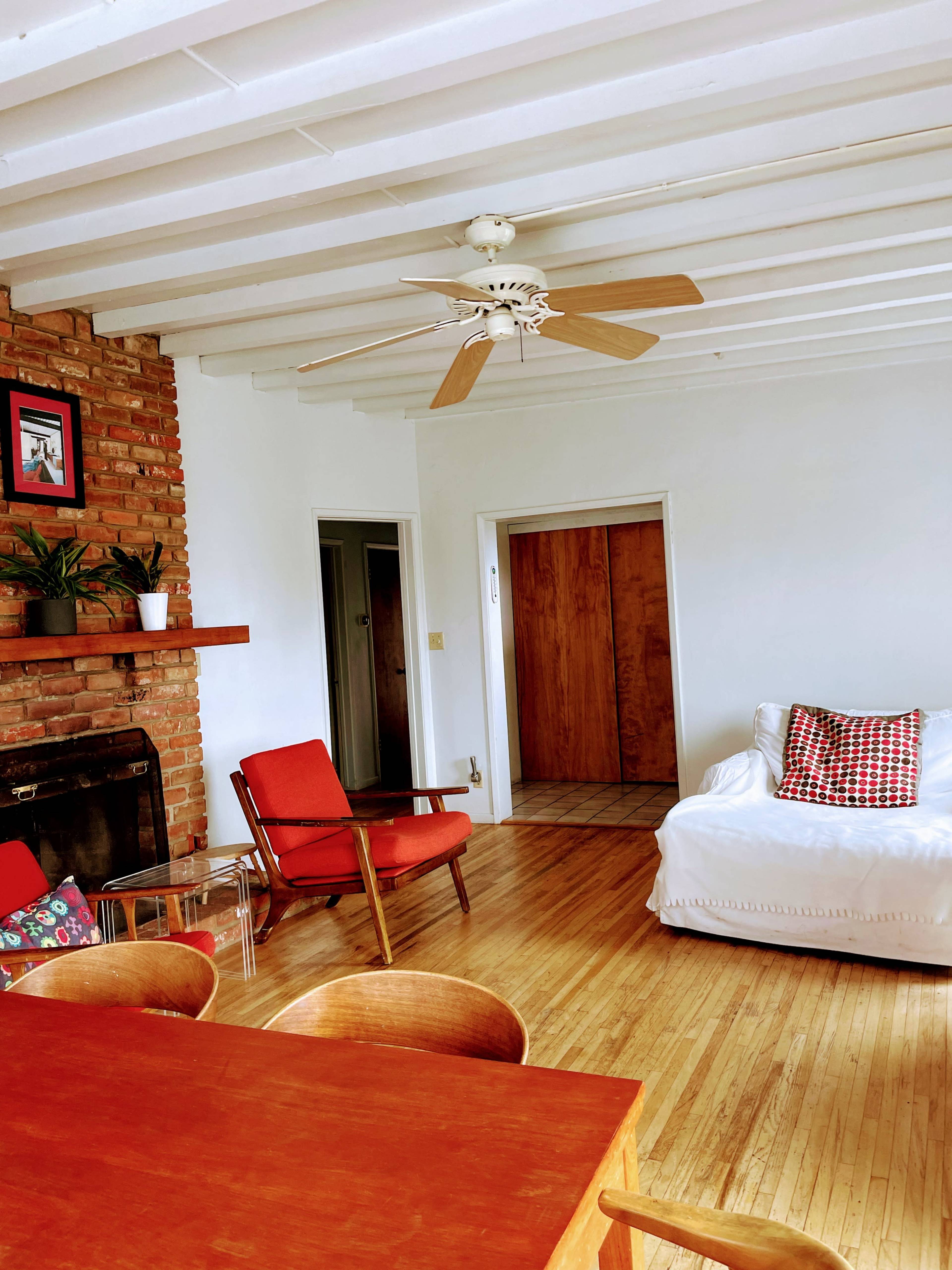 A minimalist living room with wooden floors, a brick fireplace, and a mix of red and white furniture.