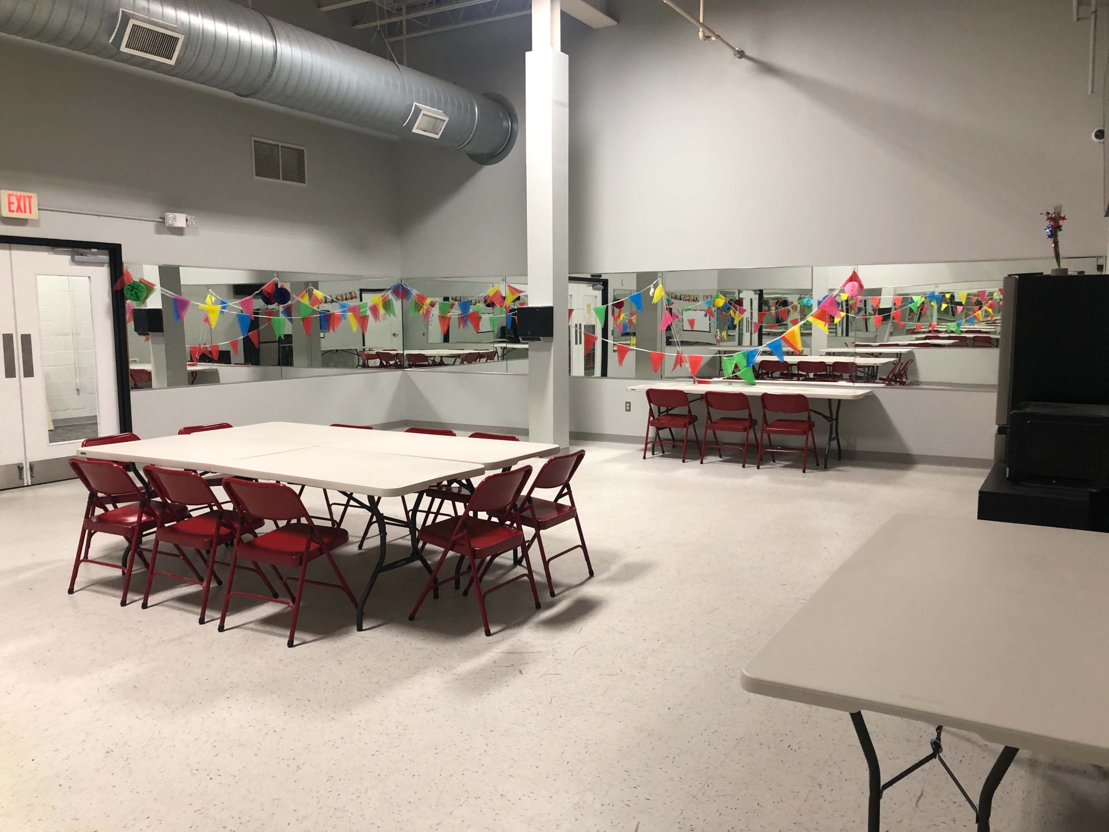 The image shows a large, empty room with red folding chairs arranged around several tables and colorful banners hanging along the walls.