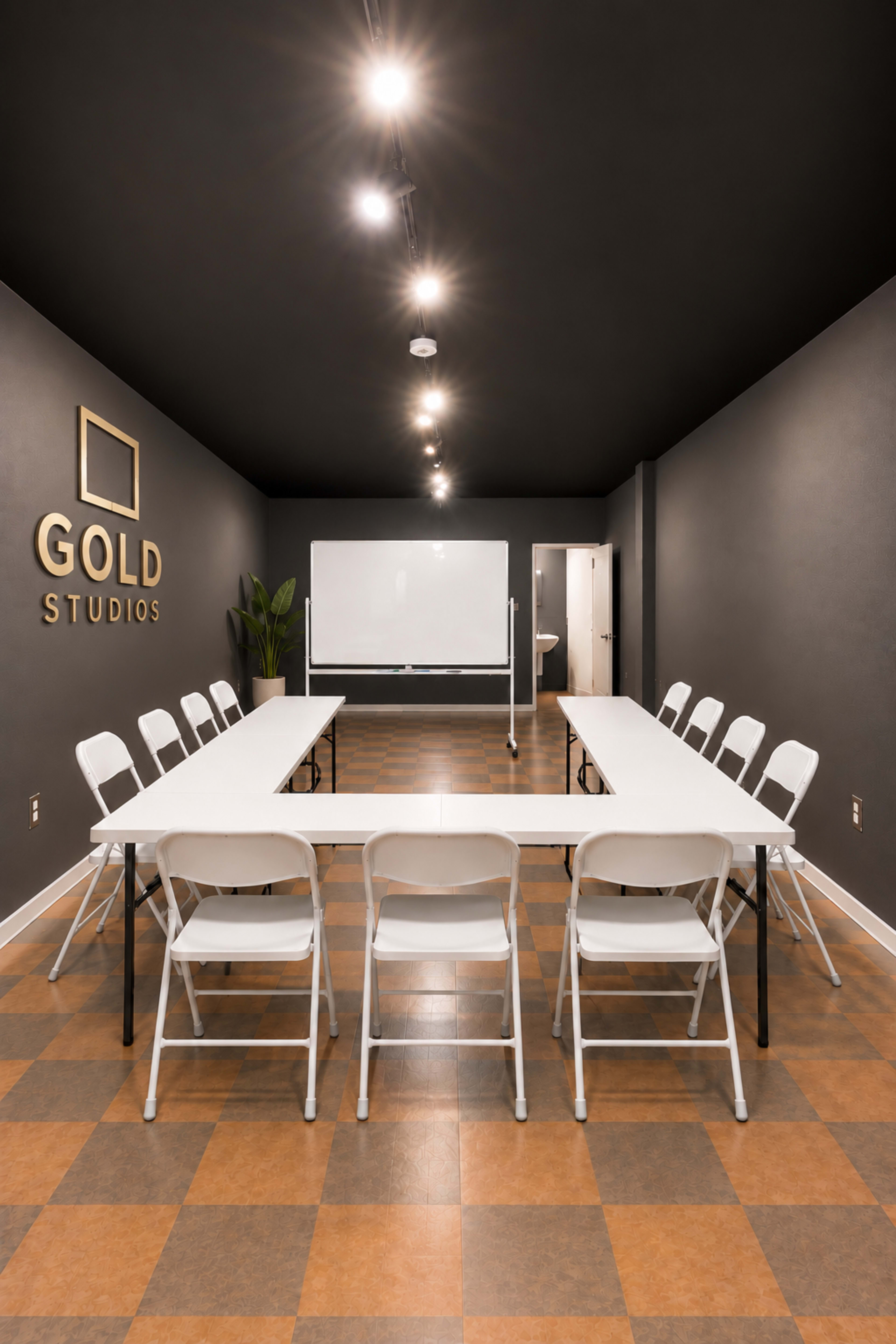 A conference room features a rectangular table surrounded by folding chairs, with a whiteboard and a door in the background.