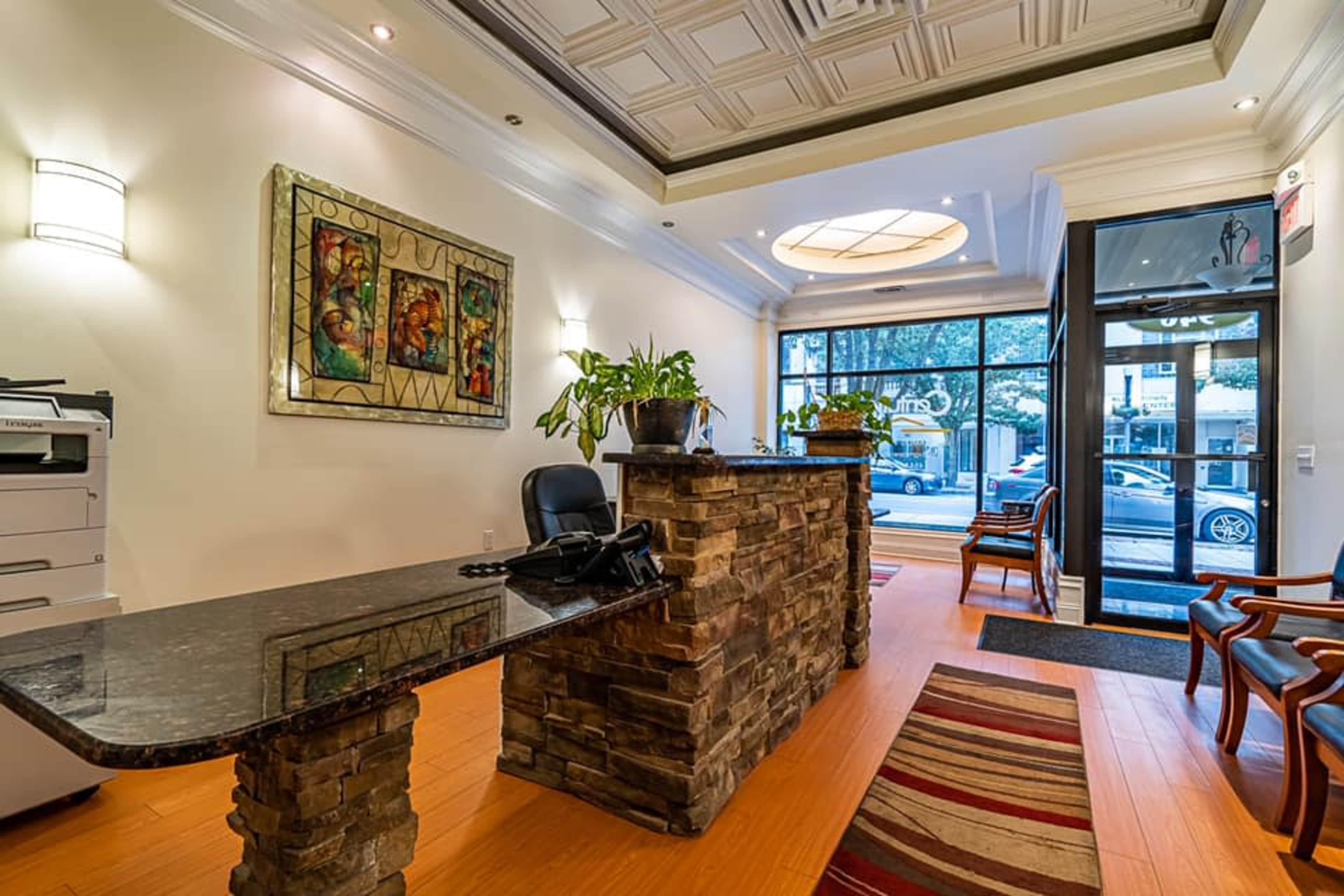 The image shows a modern reception area featuring a stone-front desk, a large artwork on the wall, and several chairs arranged around a rug.