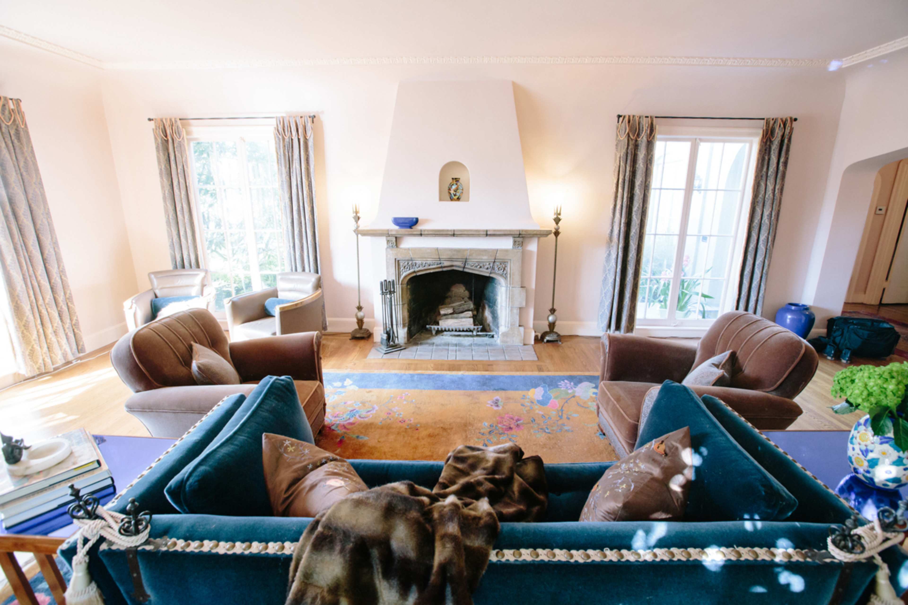 The image shows a cozy living room with a fireplace, two armchairs, and a blue sofa situated centrally in front of the fireplace.