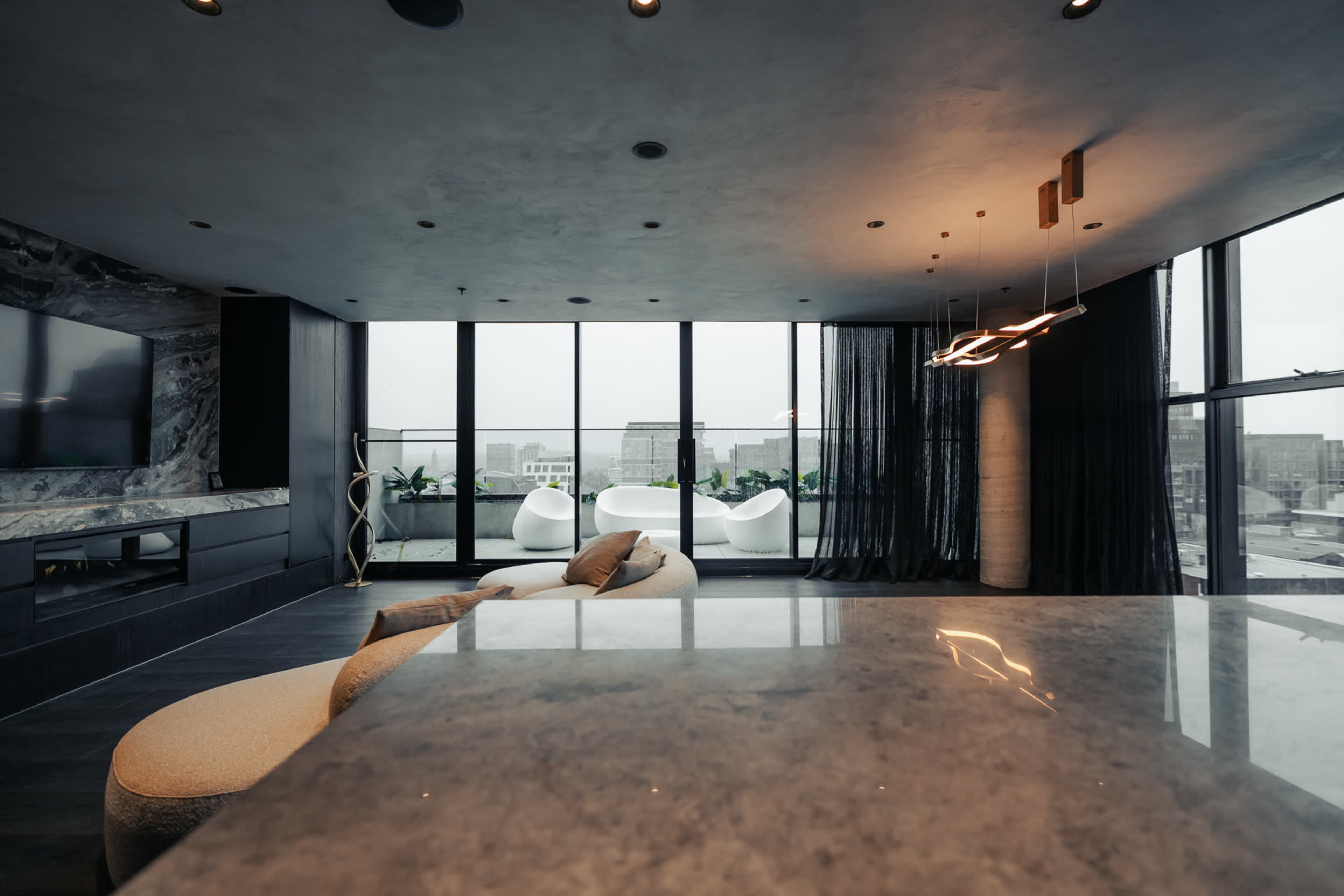 The image shows a modern living space with large windows, minimalist furniture, and a sleek kitchen counter.