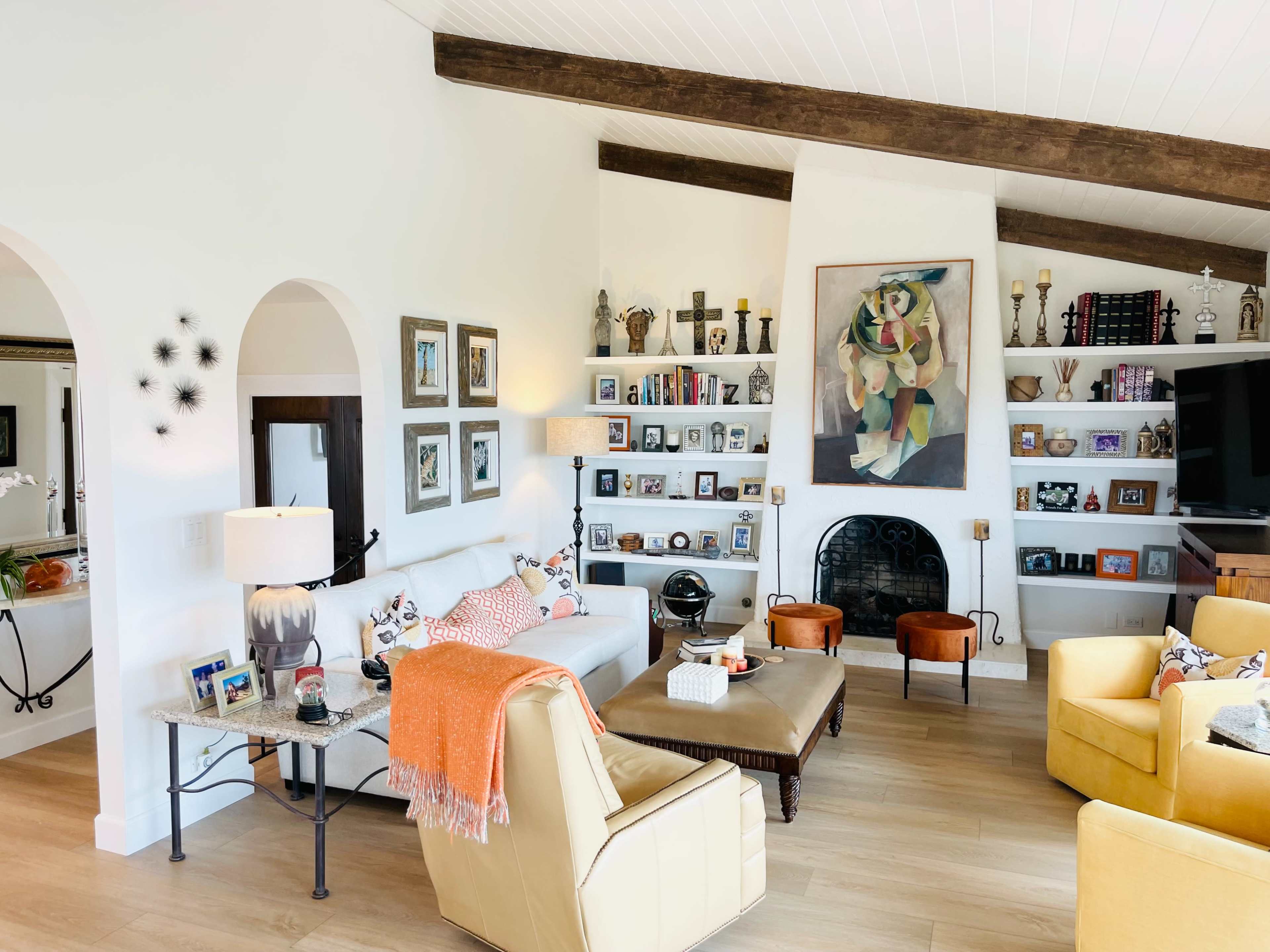 A spacious living room features a mix of seating arrangements, a fireplace, shelves filled with photos and decor, and large windows providing natural light.