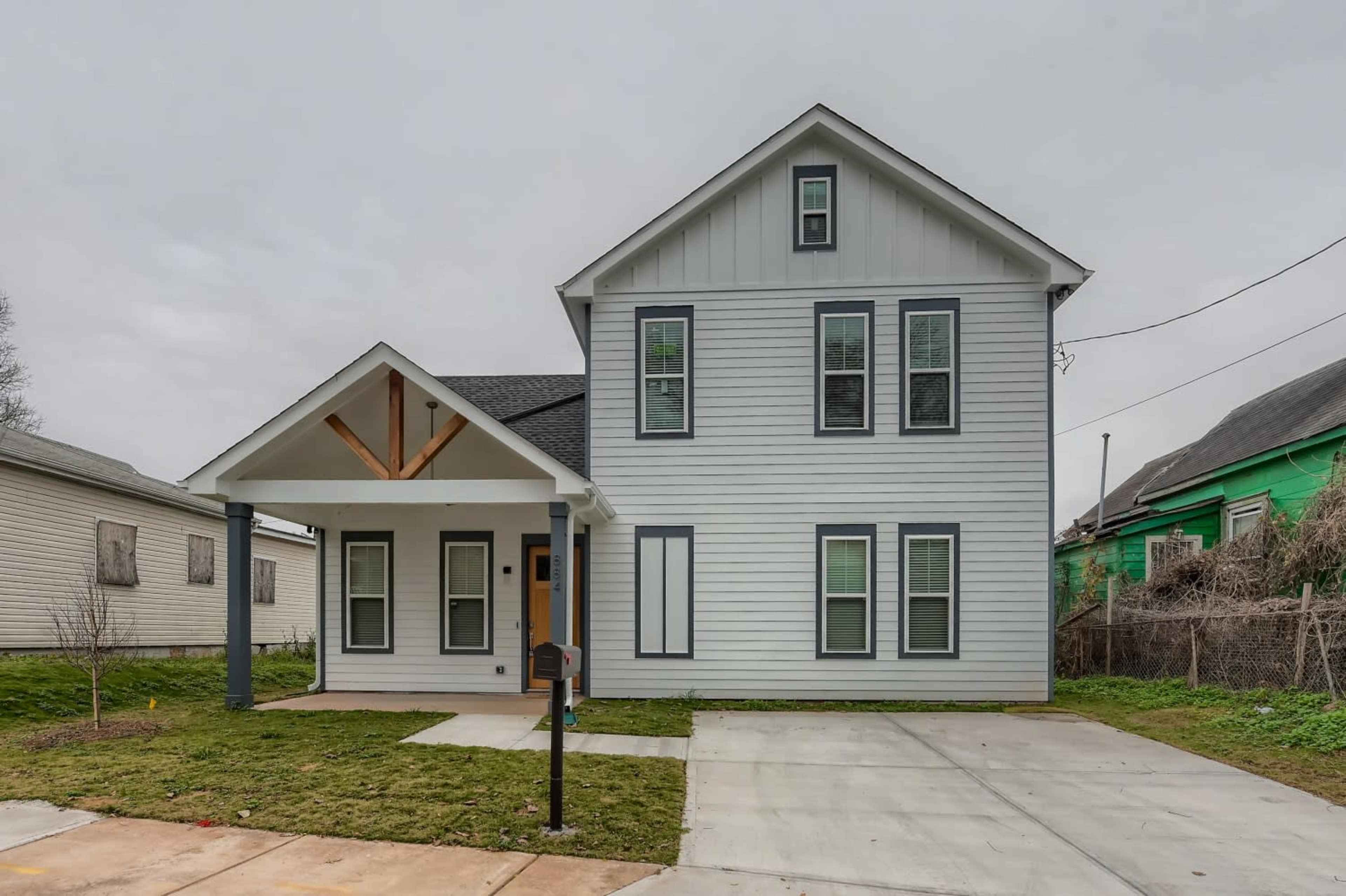 A two-story house with a gray exterior, a front porch supported by two columns, and a concrete driveway.
