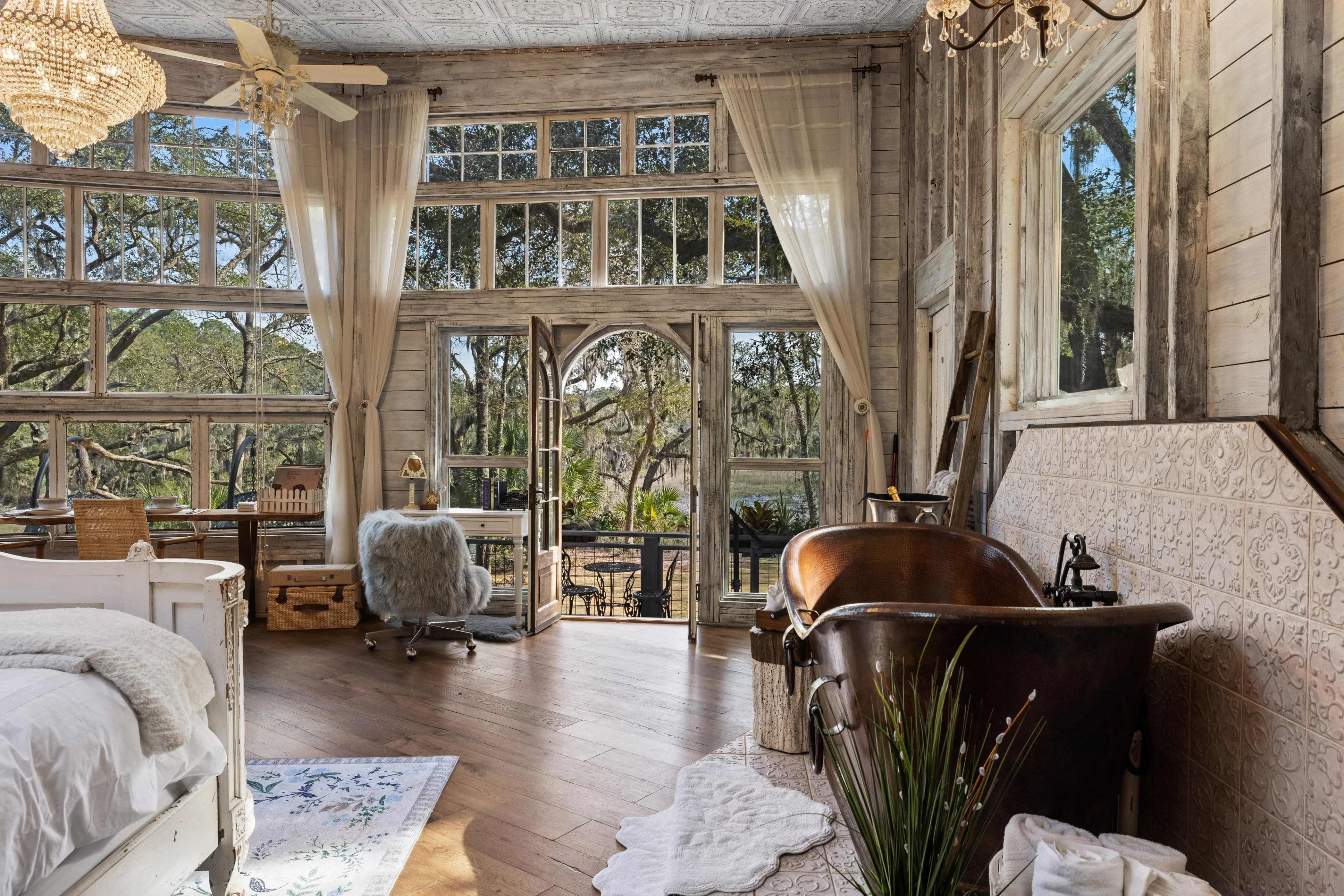 A spacious room features large windows, a freestanding bathtub, and wooden flooring, seamlessly connecting indoor and outdoor views.
