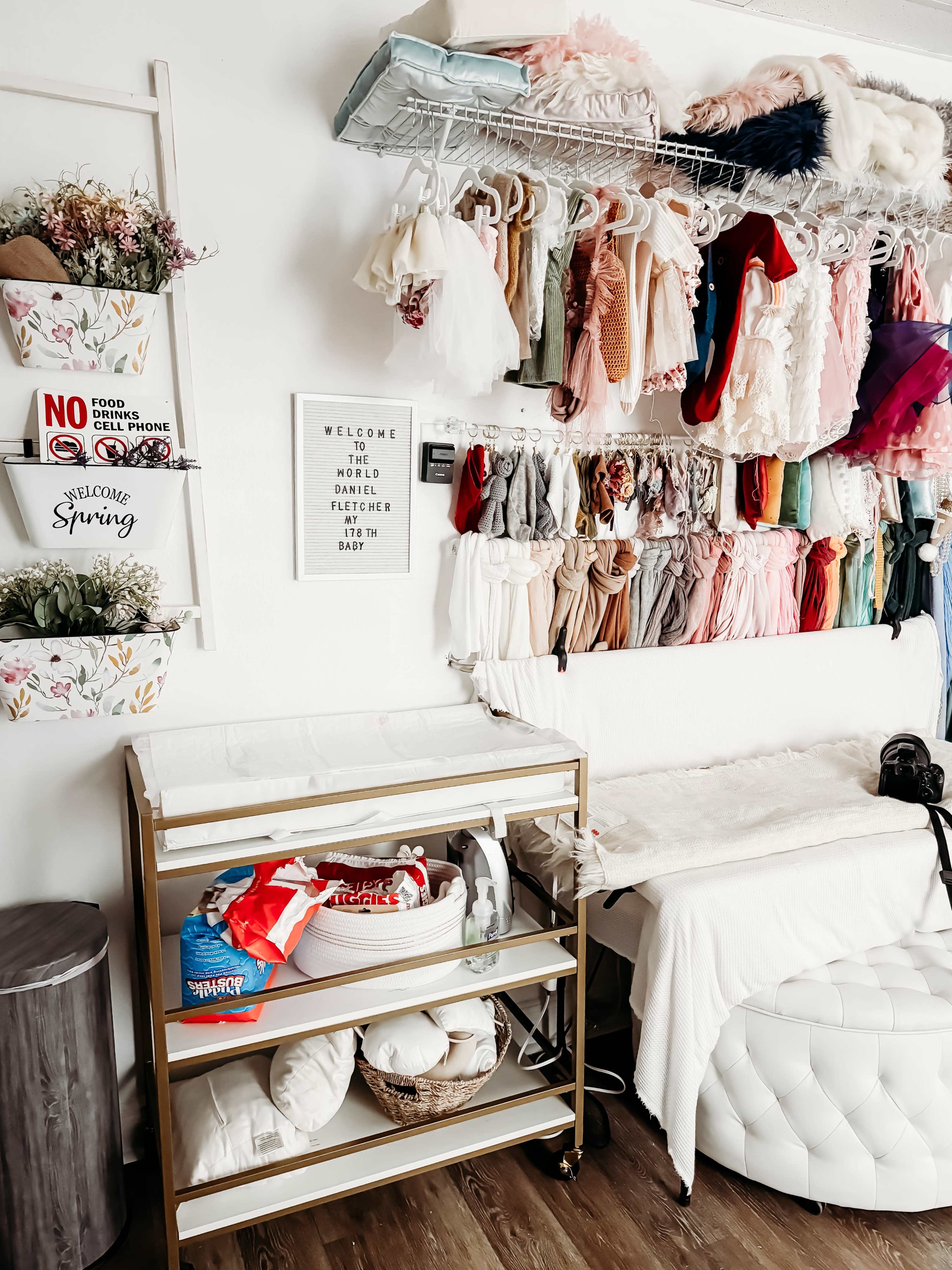 A neatly organized room featuring a rack of colorful costumes and a cart with storage bins, alongside a white seating area and decorative wall signs.