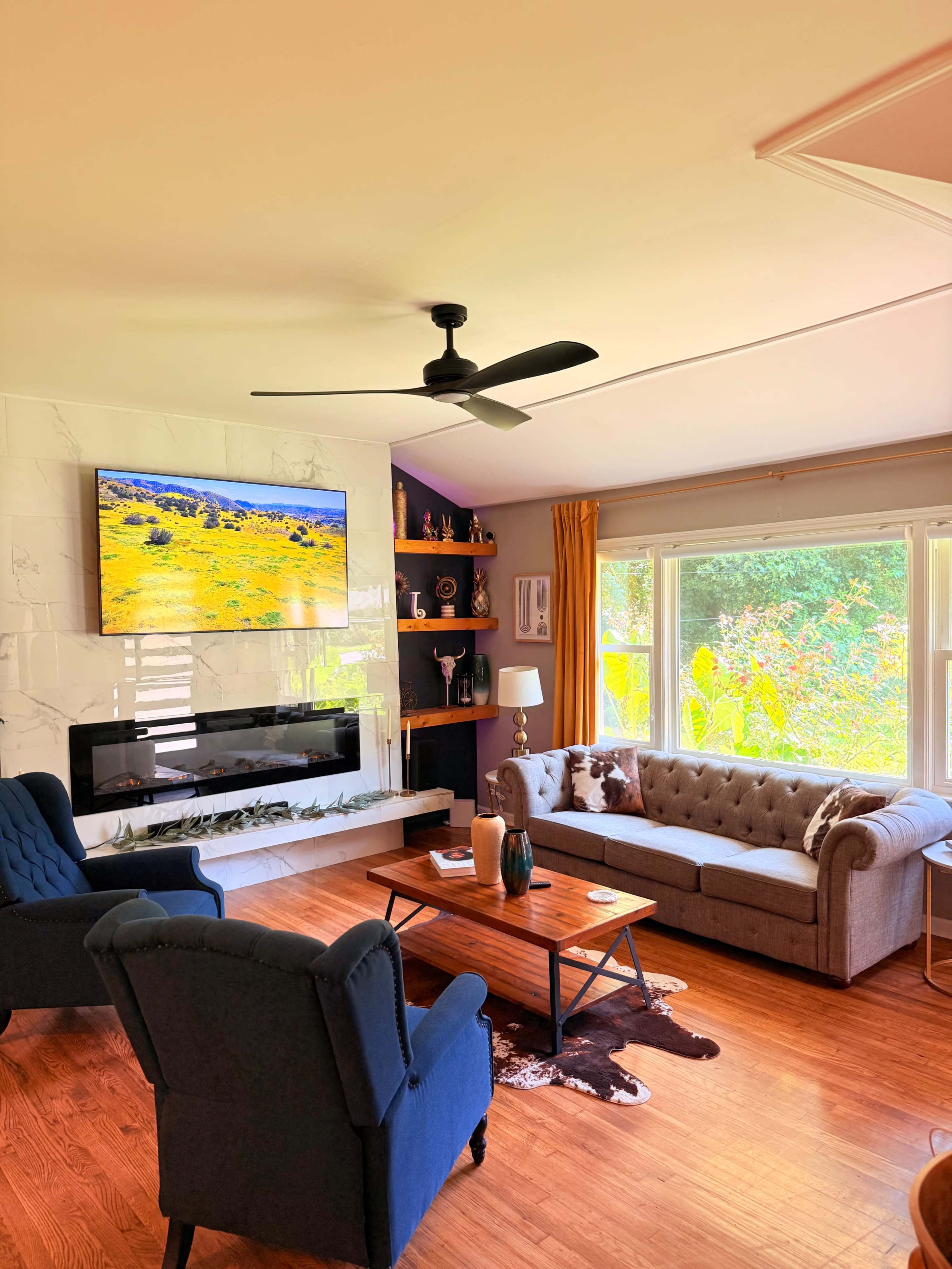 The living room features a television mounted on the wall above a modern fireplace, with a couch and two armchairs arranged around a wooden coffee table.