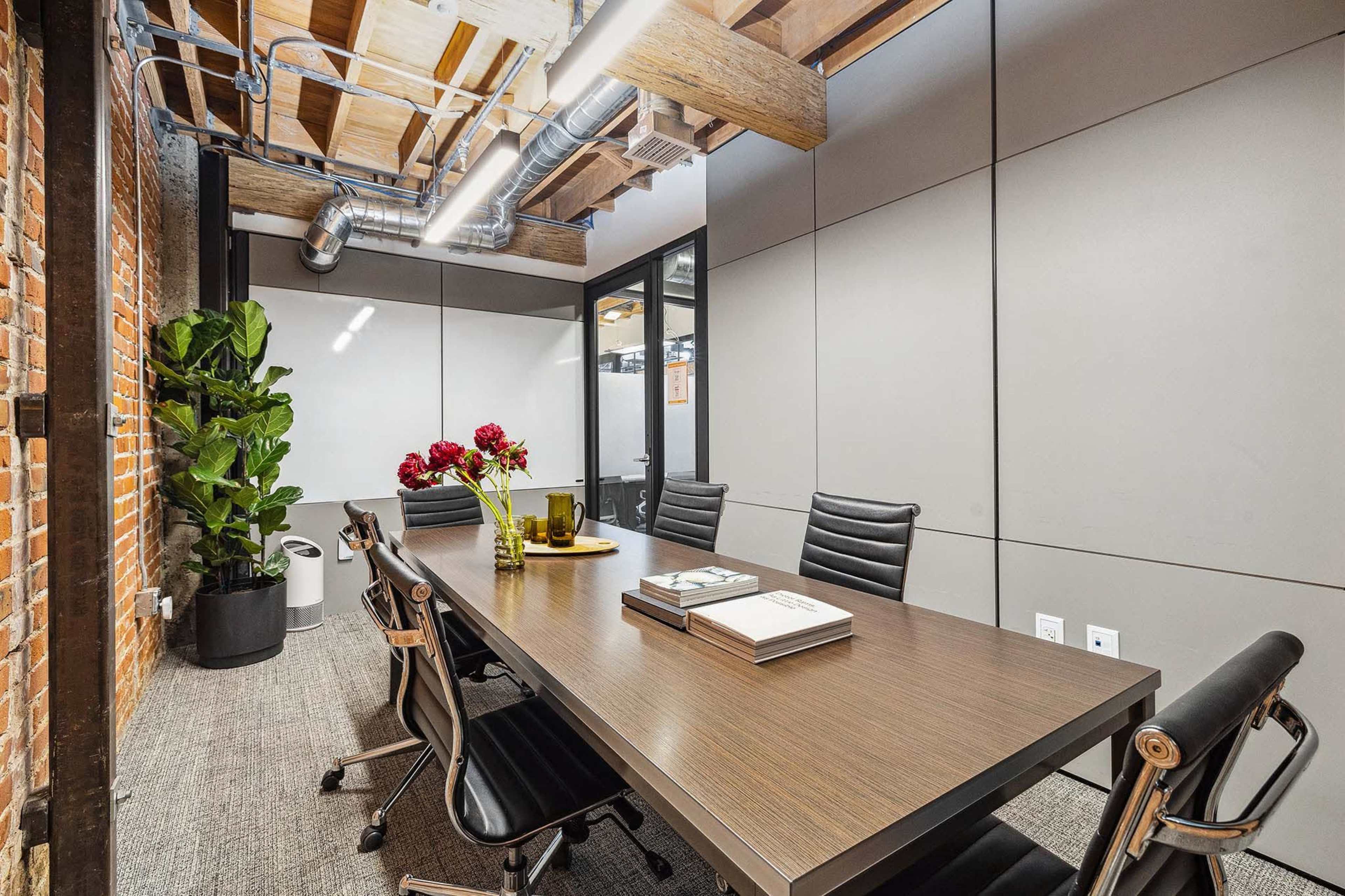 A conference room features a long wooden table with several black chairs, surrounded by exposed brick walls and modern lighting.