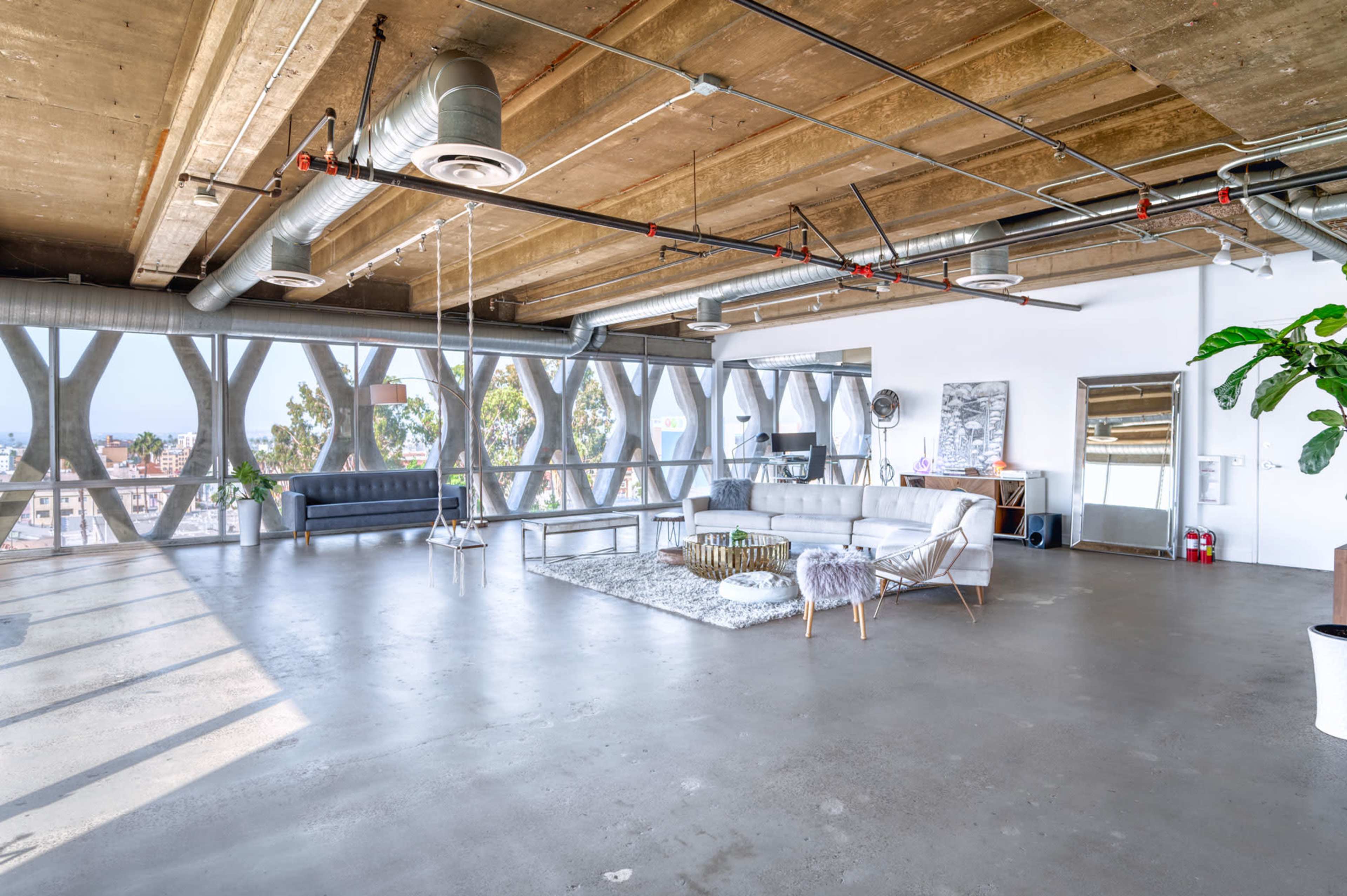 The spacious interior features industrial-style ceilings and large windows, creating an open area with modern furniture and a minimalist aesthetic.