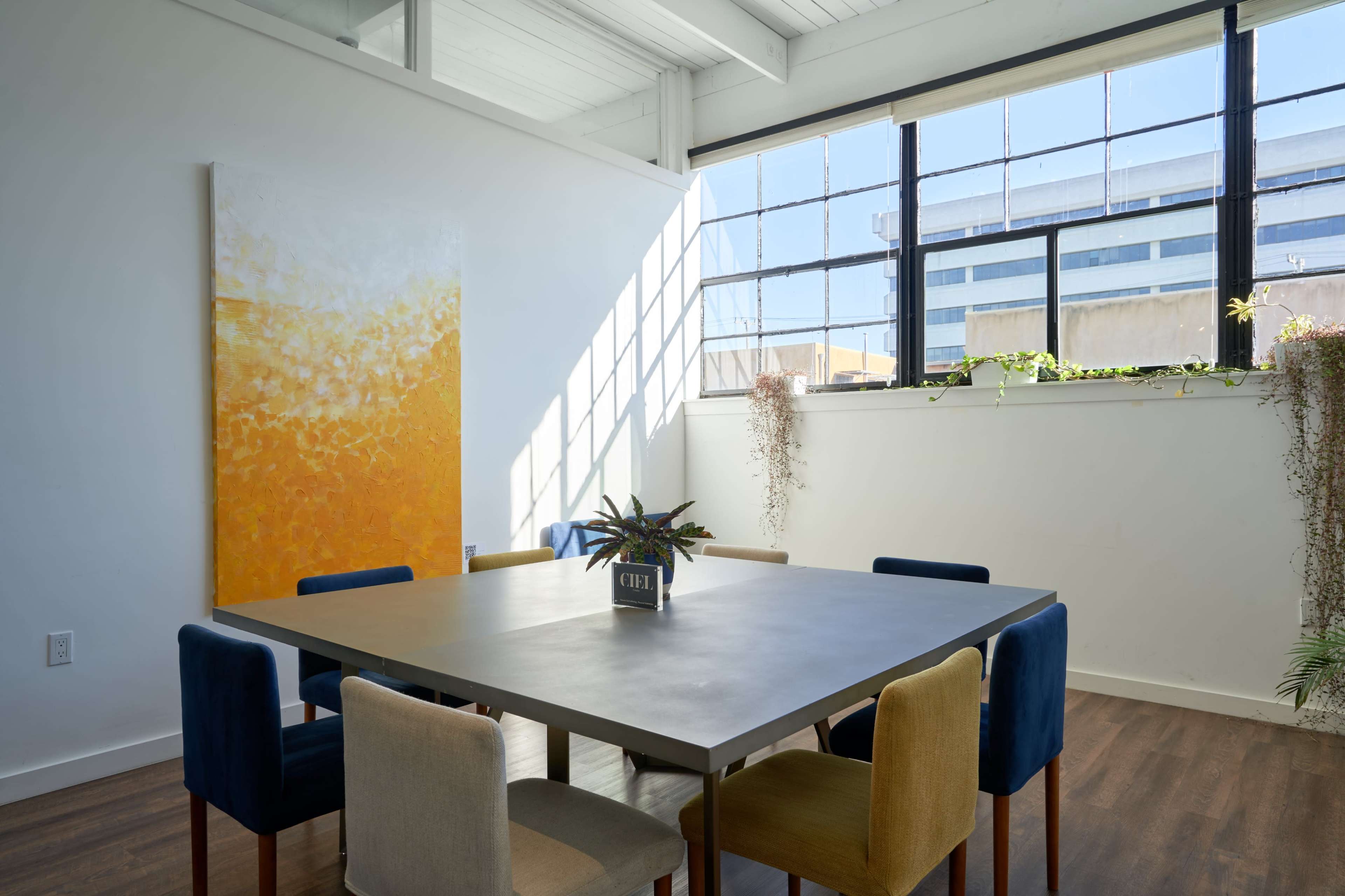 A bright, modern dining area with a large table surrounded by chairs of different colors and a large window letting in natural light.