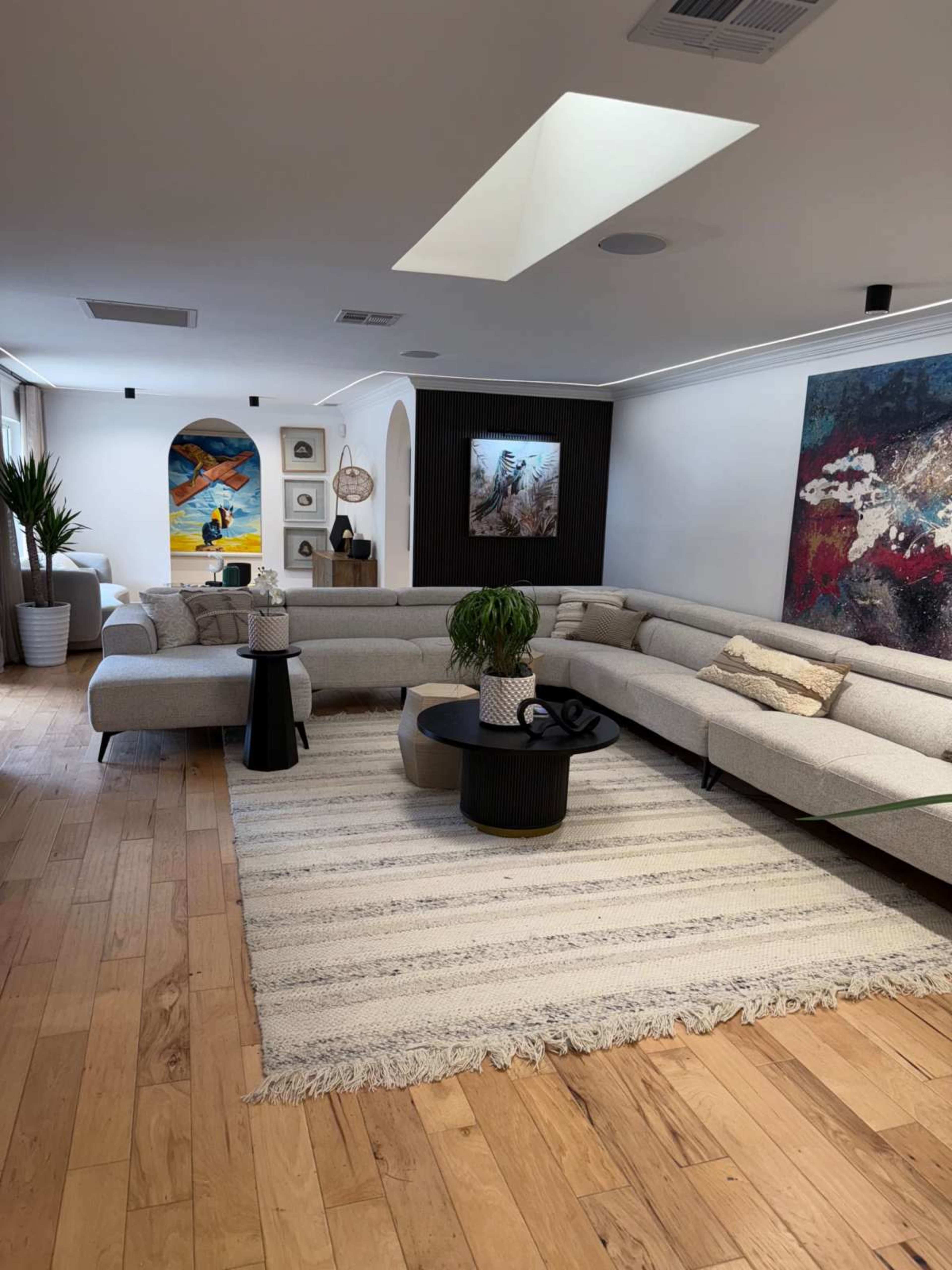 The living room features a large sectional sofa, a round coffee table, artworks on the walls, and a wooden floor.
