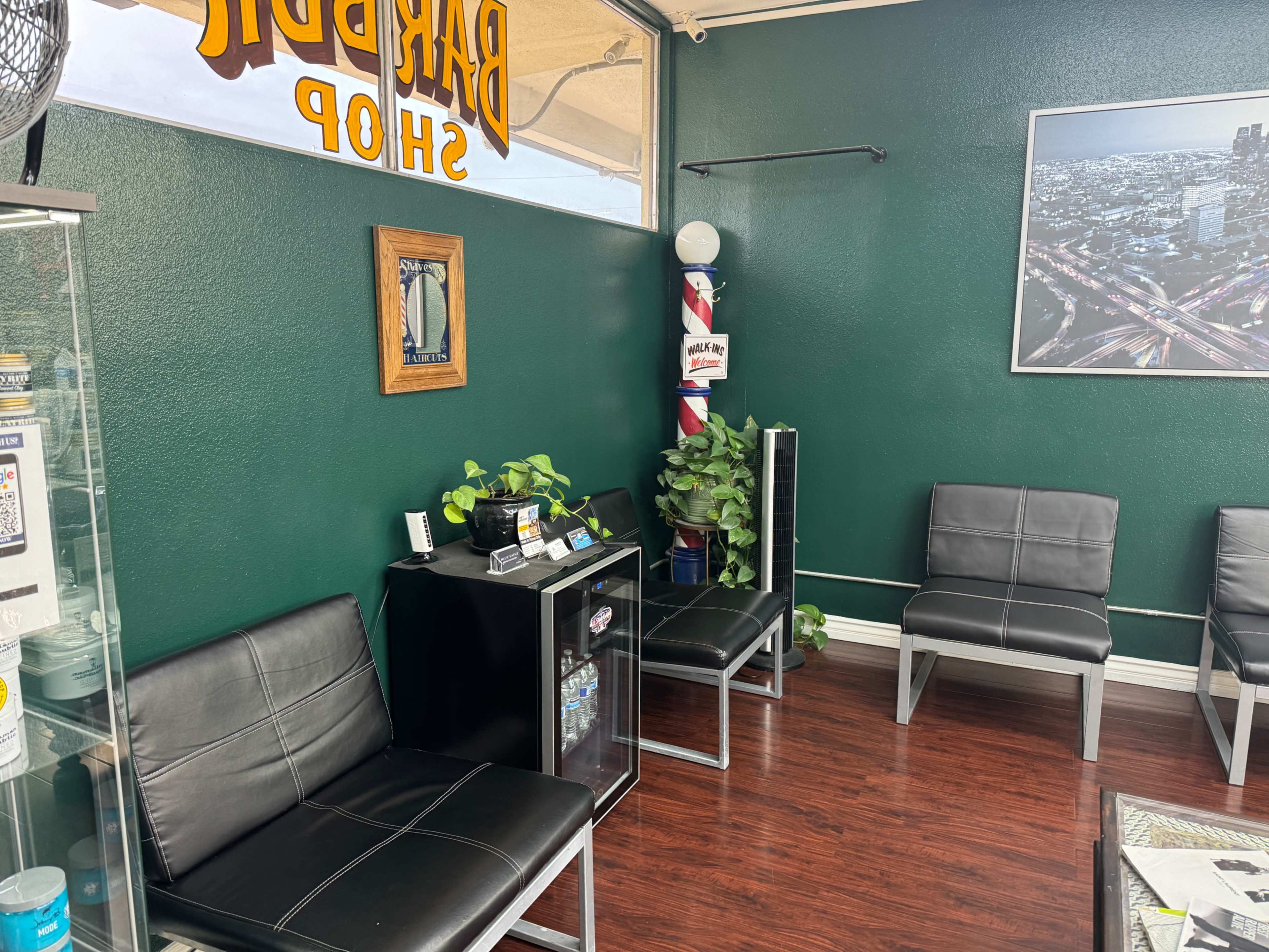The image shows the interior of a barbershop with black leather seating, a small black cabinet, and green walls.