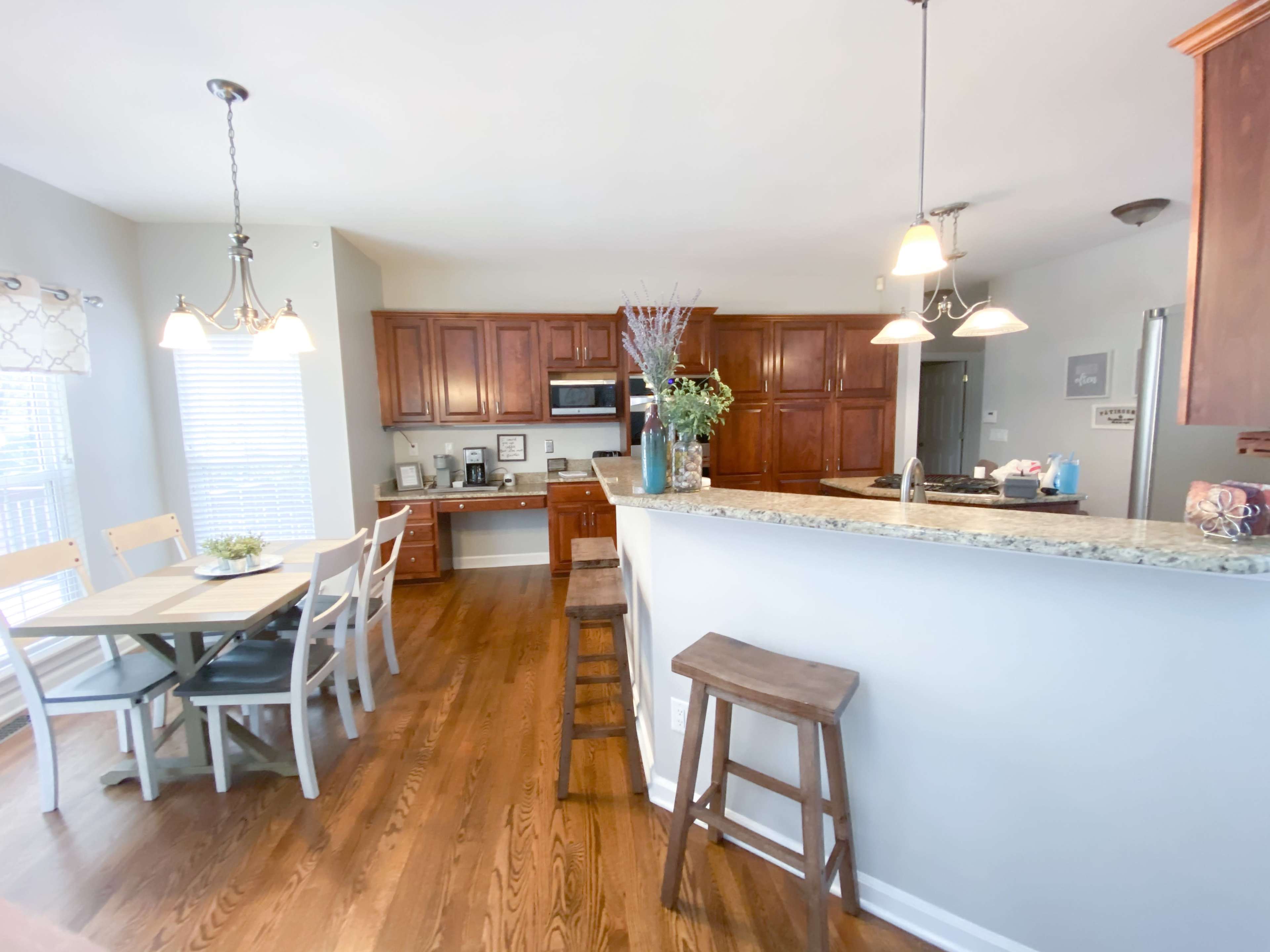 A kitchen and dining area with wooden cabinets, a granite countertop, a table and chairs, and bar stools.