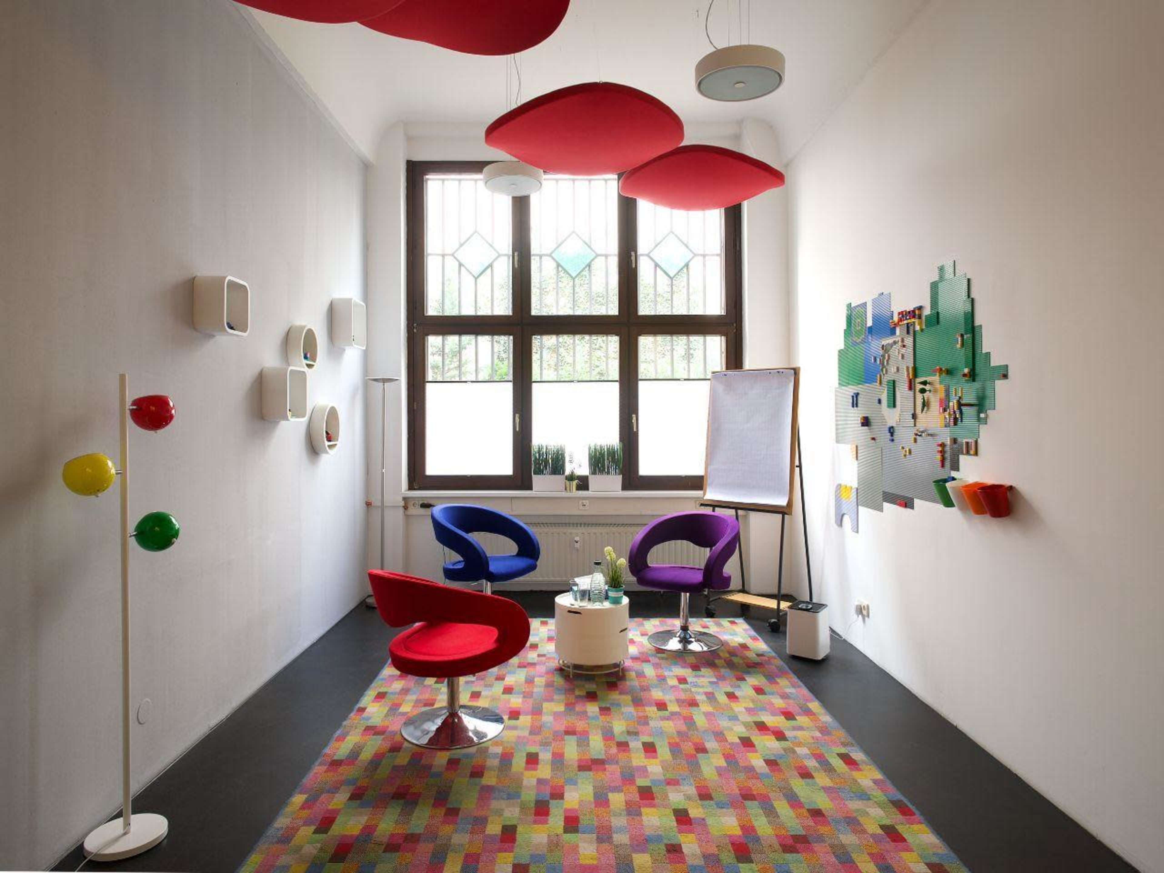 A modern meeting room features colorful furniture, a patterned rug, and large windows providing natural light.