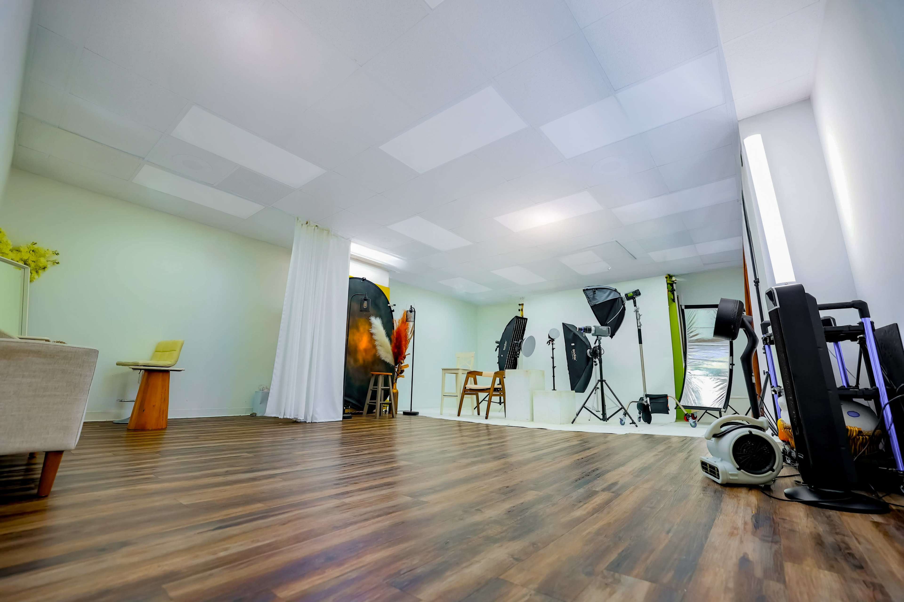 The image depicts a spacious photography studio featuring various lighting equipment, backdrops, and props arranged throughout the room.