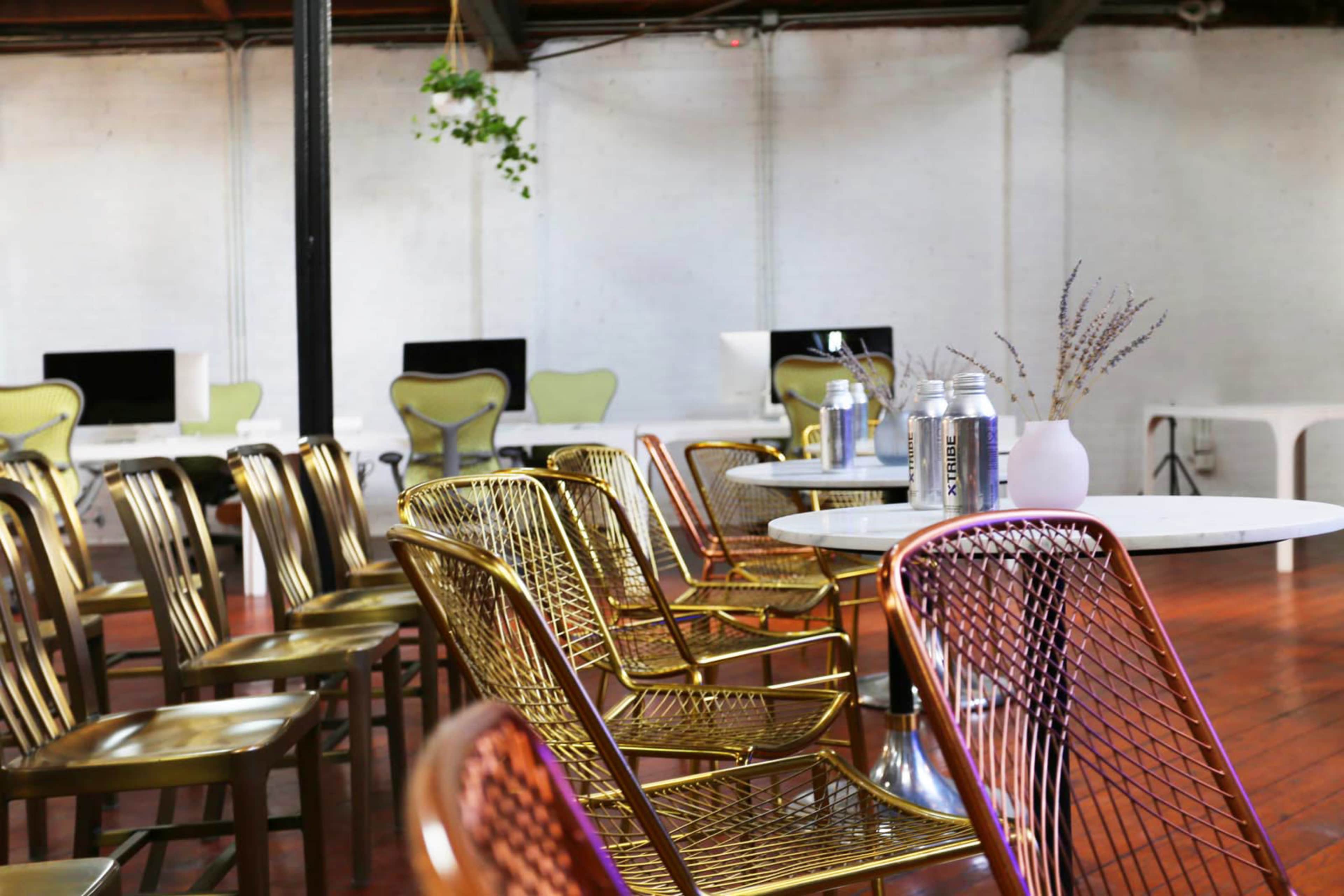 A modern interior features gold and copper wire chairs arranged around tables, with computers visible in the background.