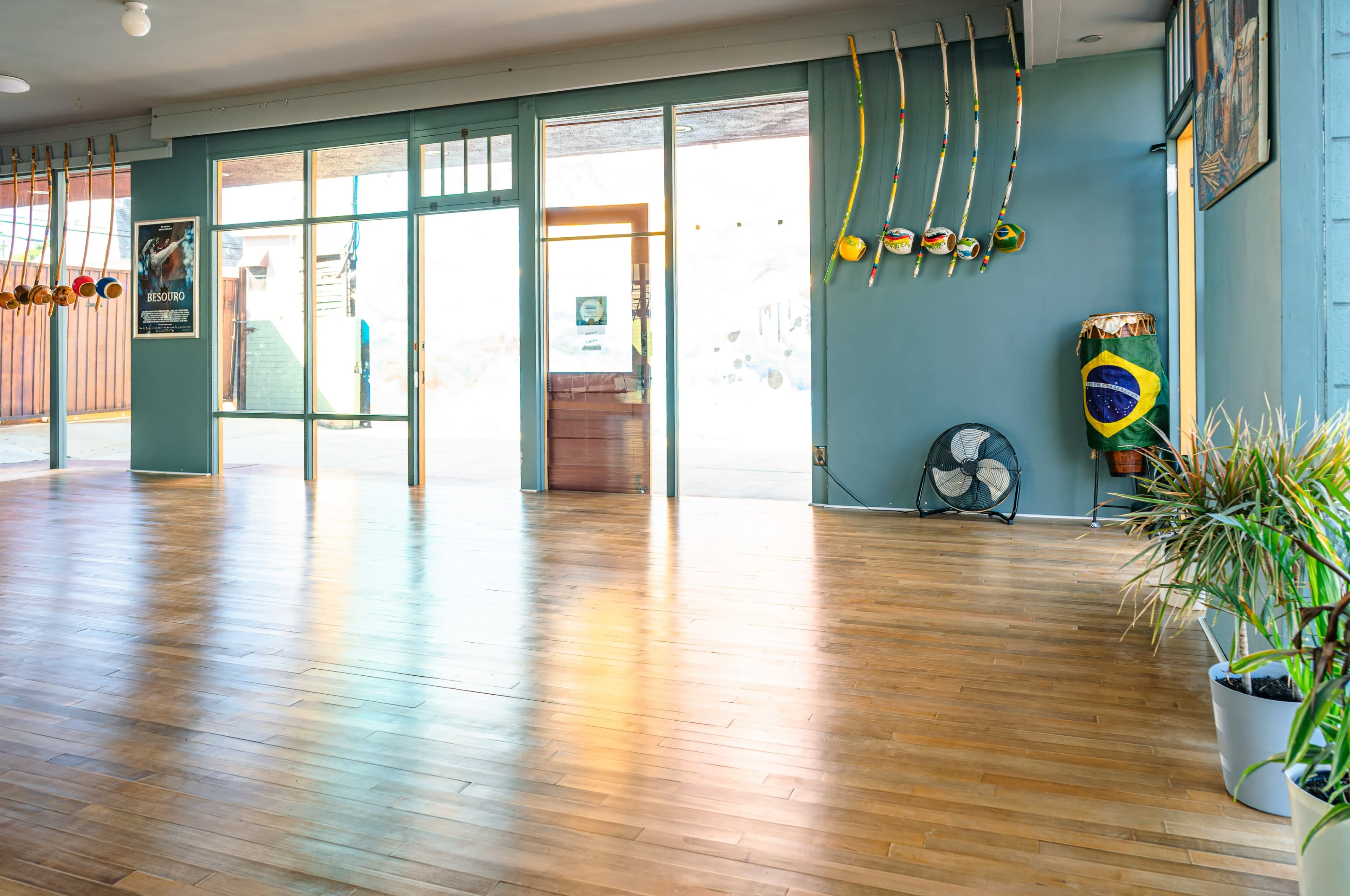 A spacious indoor area with wooden flooring, large windows allowing natural light, and various items related to a Brazilian cultural practice displayed on the walls.