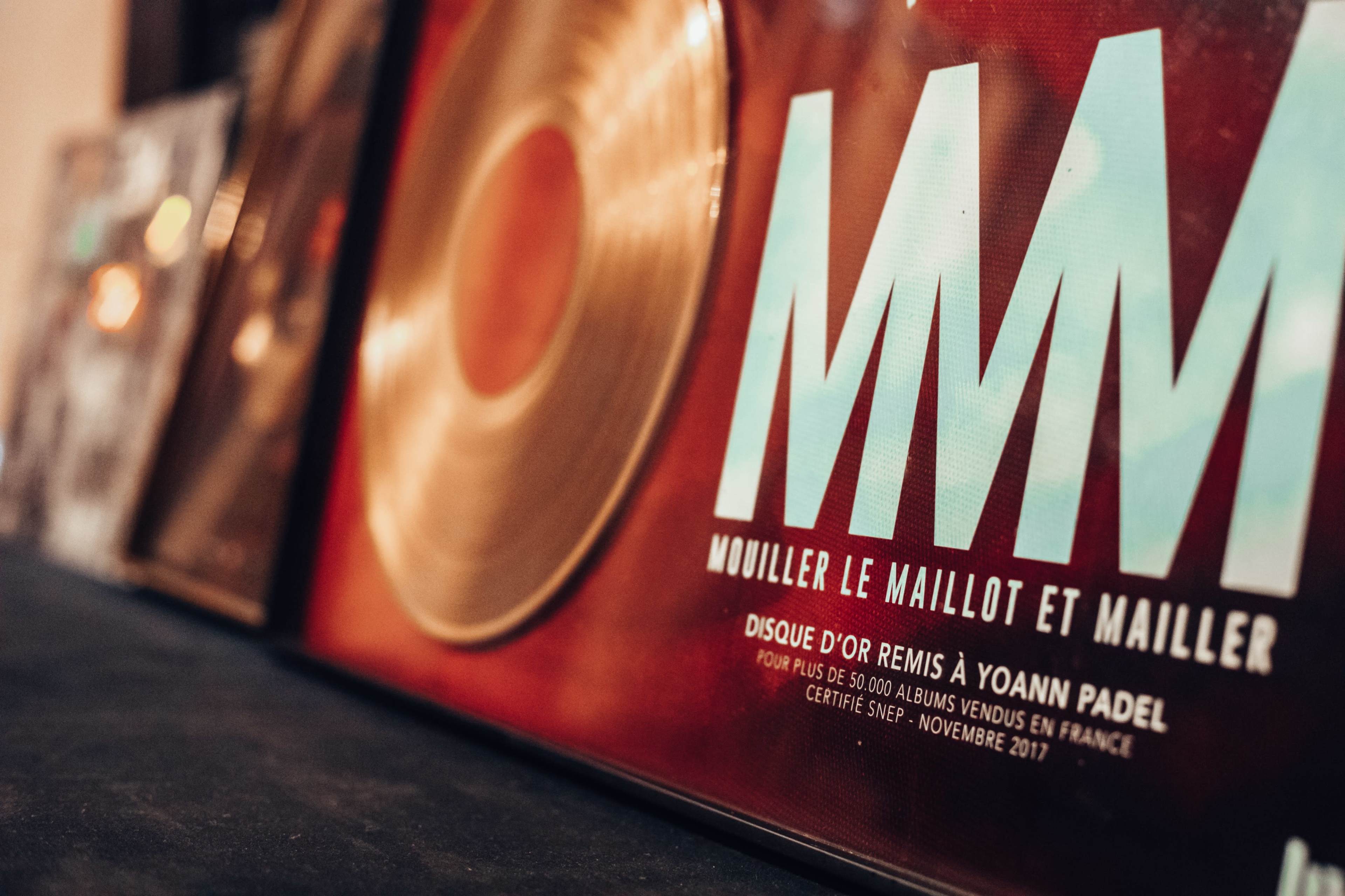 A close-up of a record display with a prominent red album cover that reads "MM" and includes text in French referencing an award presented to Yoann Padel.