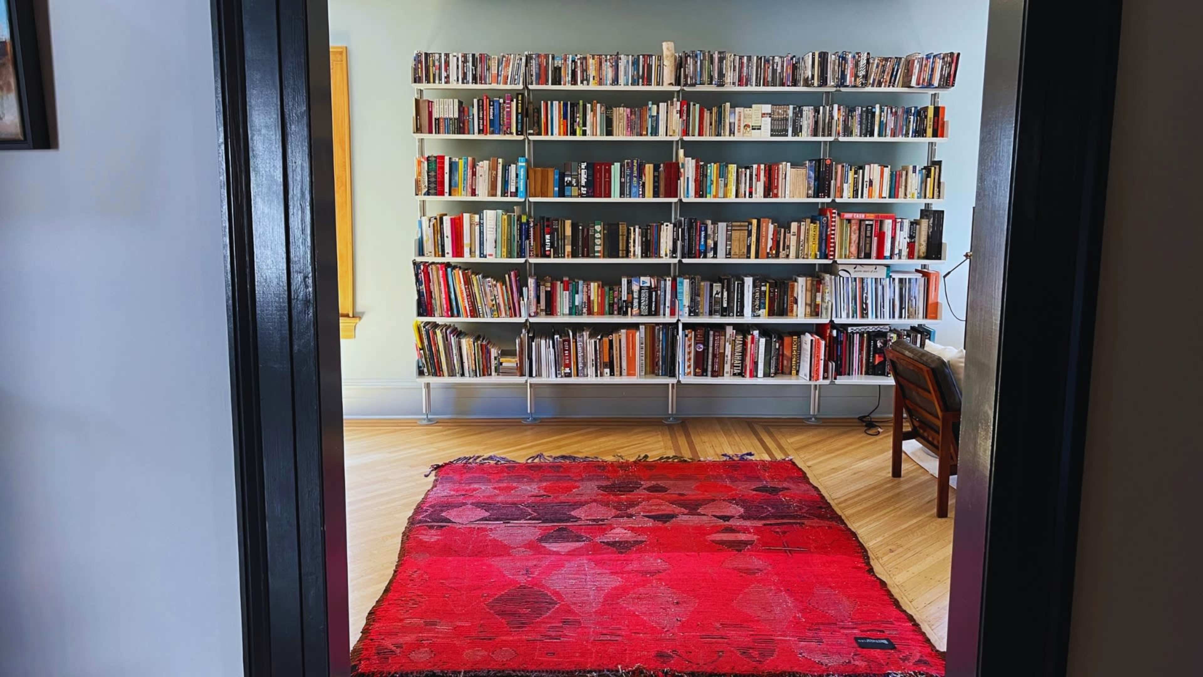 A cozy room features a large bookshelf filled with books and a red rug on the wooden floor.