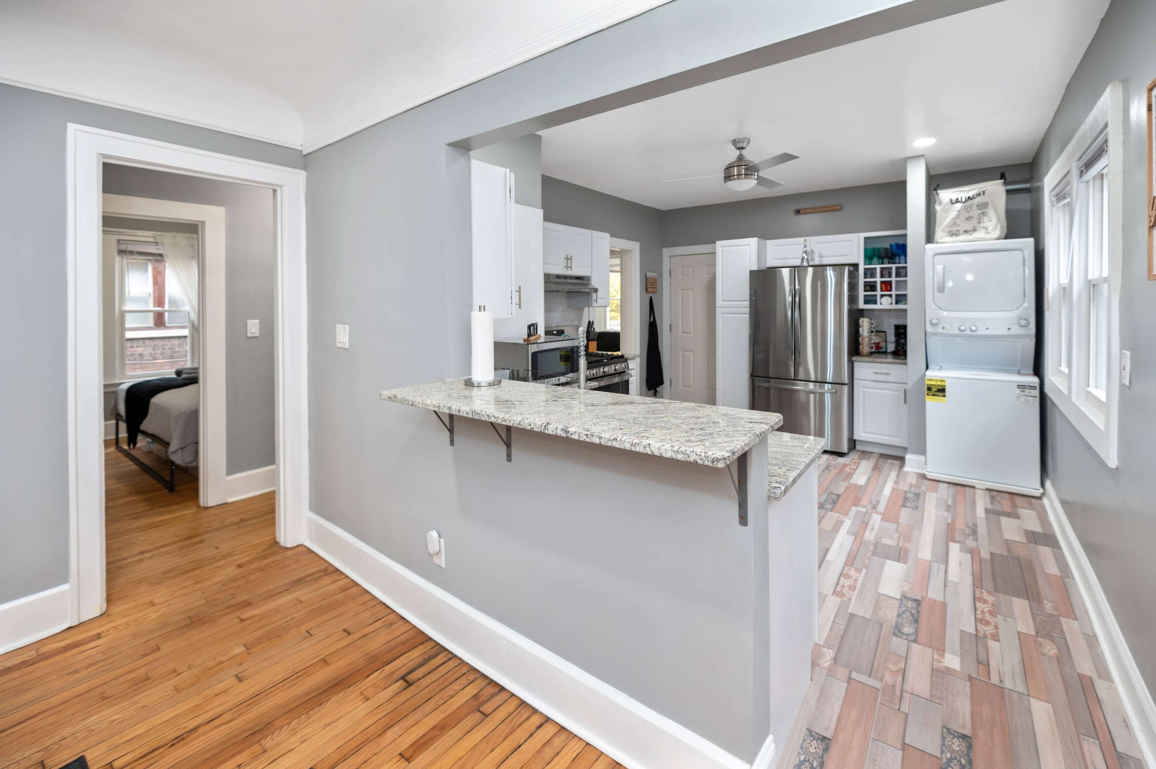 A view of a modern kitchen and hallway with hardwood flooring, granite countertops, and stainless steel appliances.