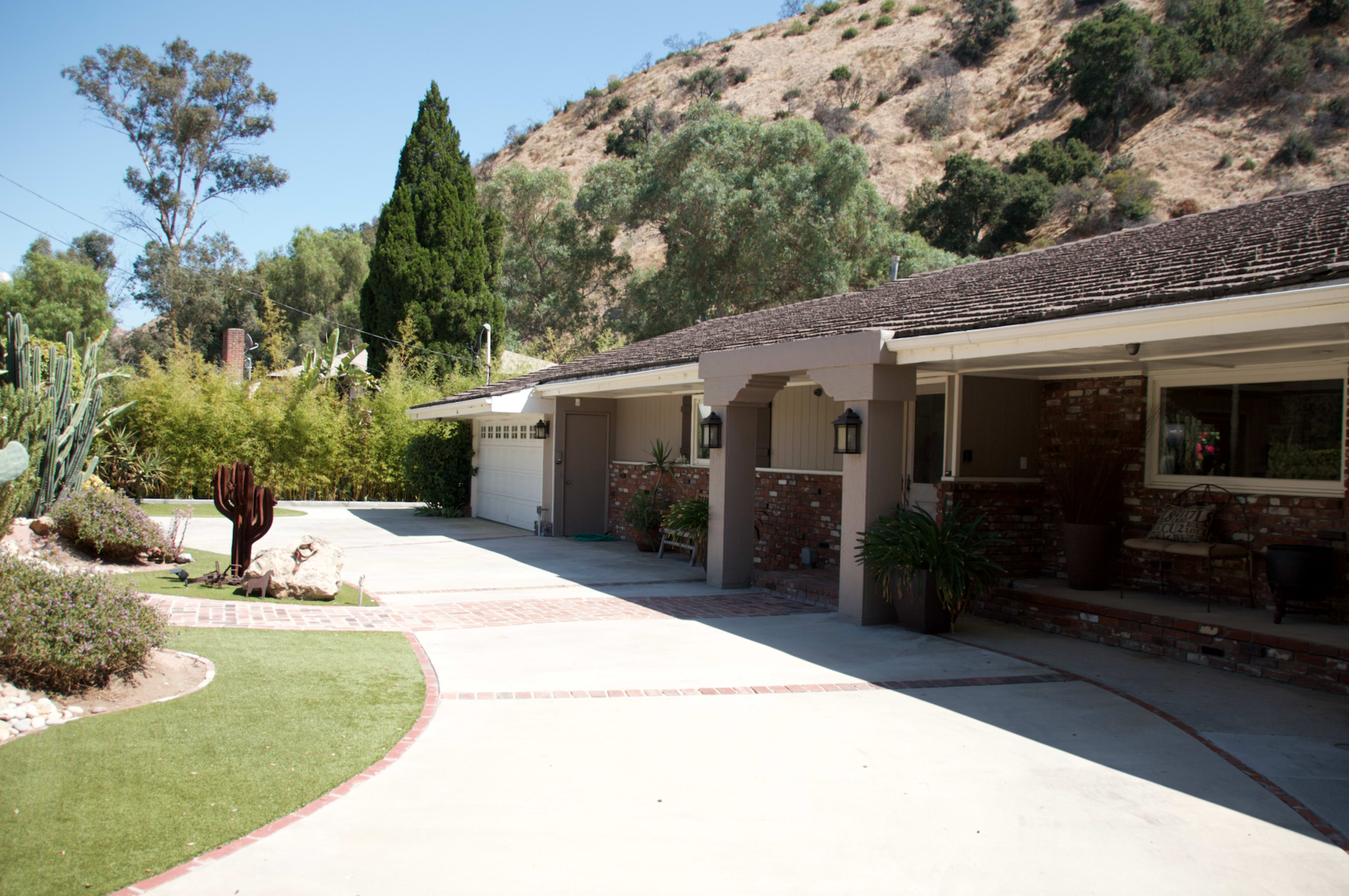 A landscaped driveway leads to a single-story home adjacent to a hillside.